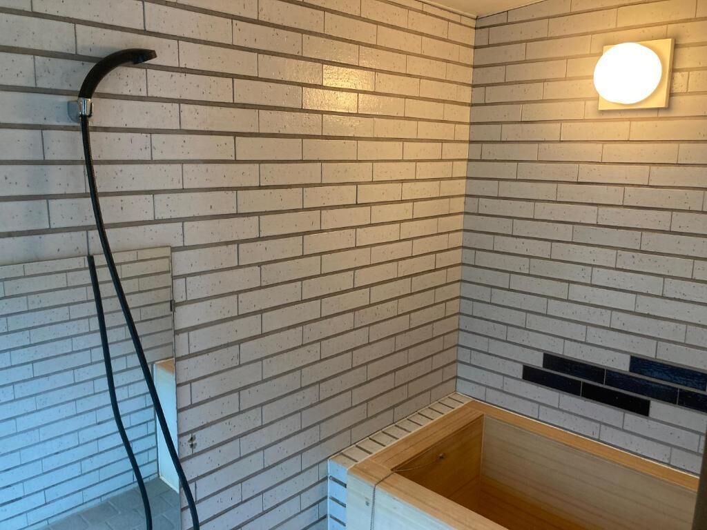 A shower area with a wooden bathtub, a black hose, and a wall-mounted light fixture.