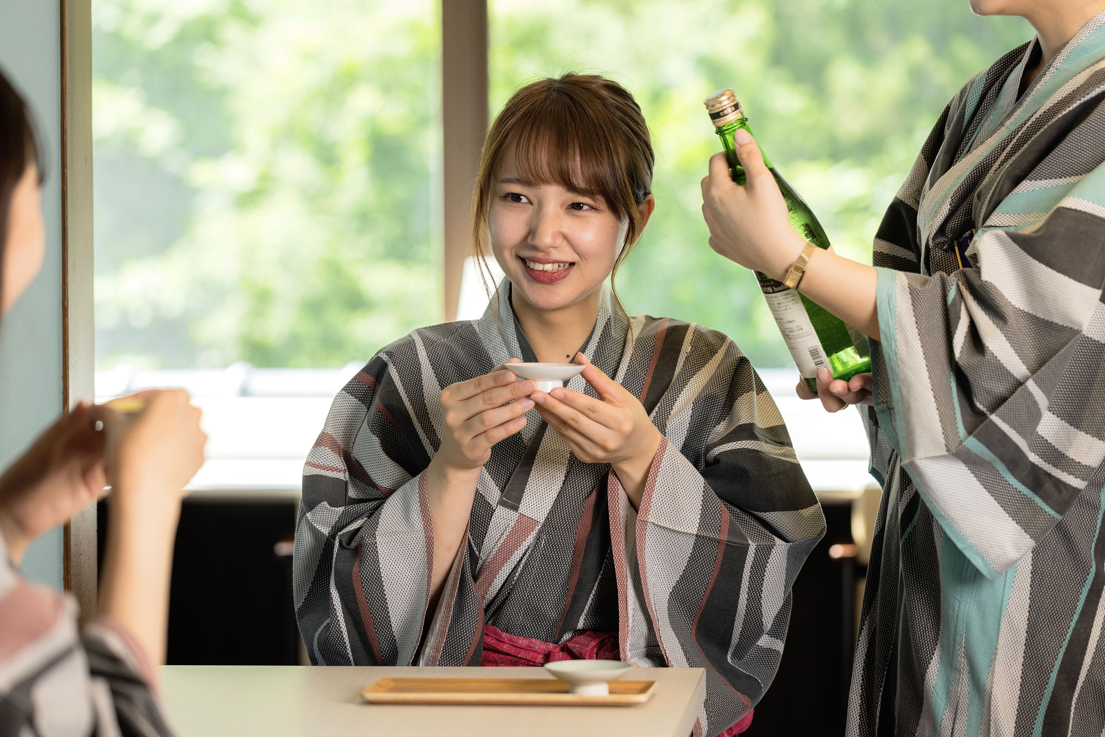 A person in a plaid robe holding a bottle, seated at a table with a cup.