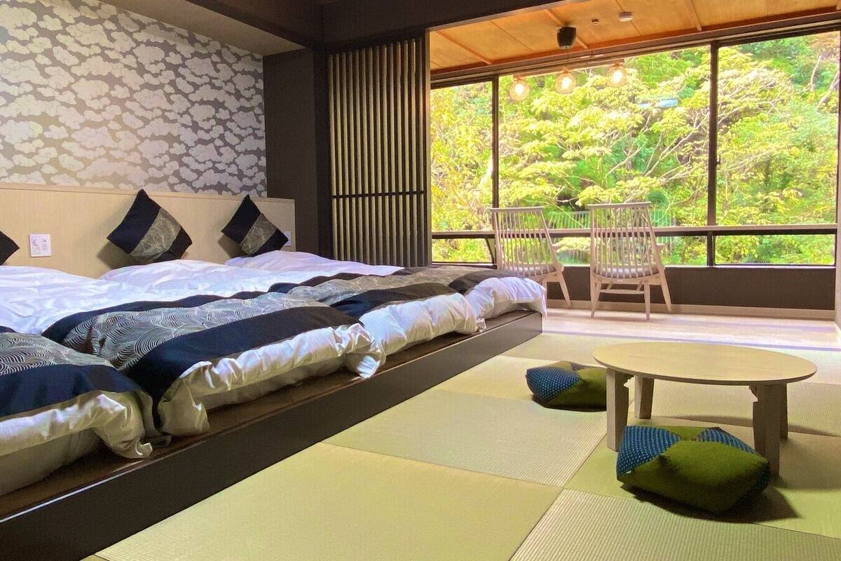 Une chambre avec un lit, une petite table et une vue sur la verdure grâce à de grandes fenêtres.