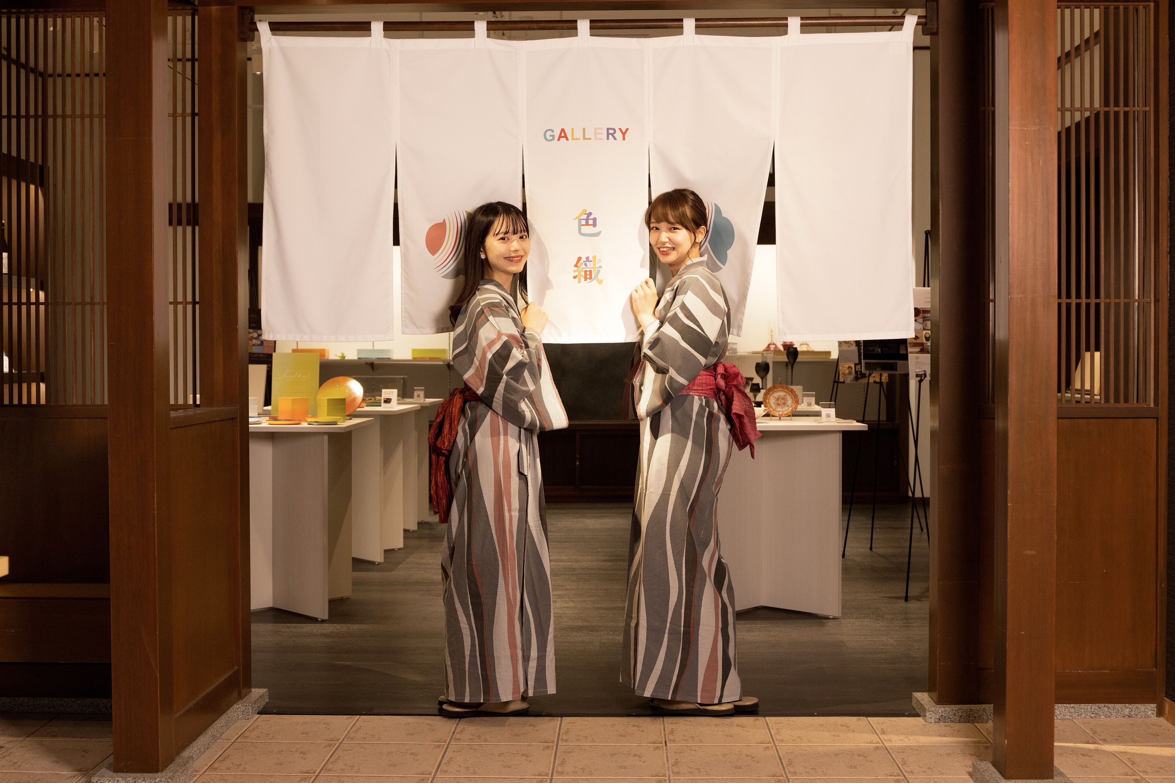 Two people standing in front of a gallery with a white backdrop and some text.
