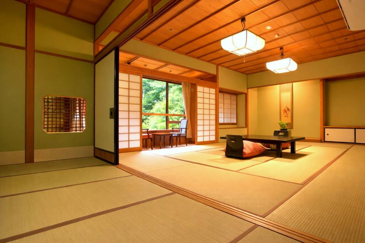 Une pièce de style japonais traditionnel, avec un sol recouvert de tatamis, une porte coulissante donnant sur un jardin et une petite table basse entourée de coussins.