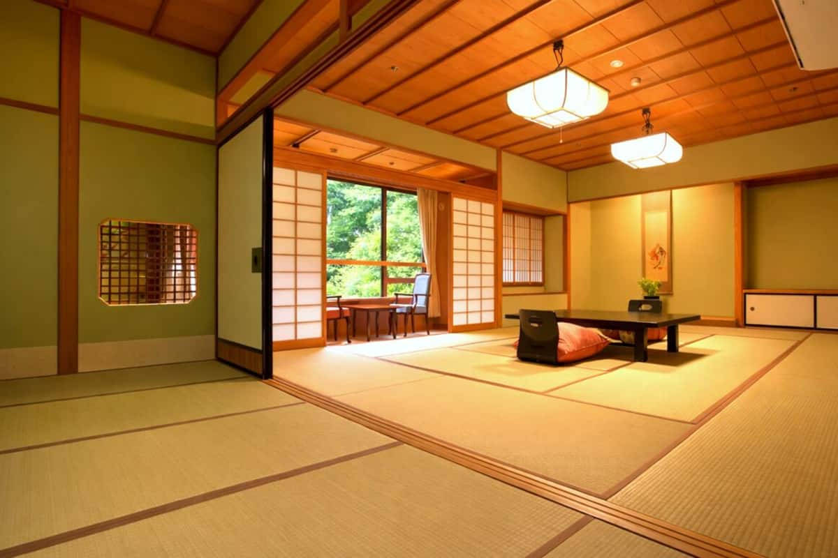 Una habitación japonesa tradicional con suelo de tatami, una puerta corredera que da a un jardín y una mesa baja con cojines.