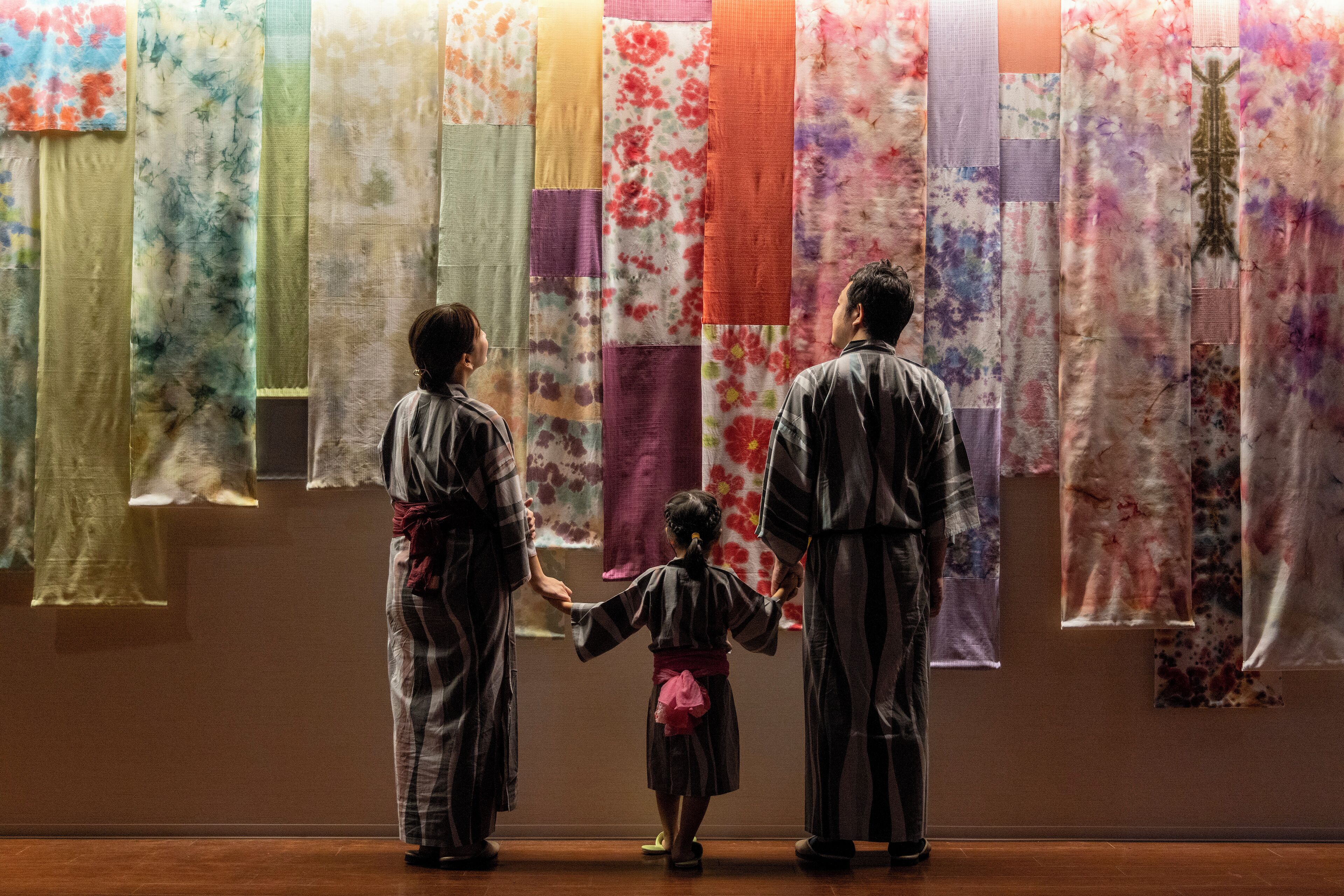 A group of people in traditional attire observing a wall of hanging fabrics.