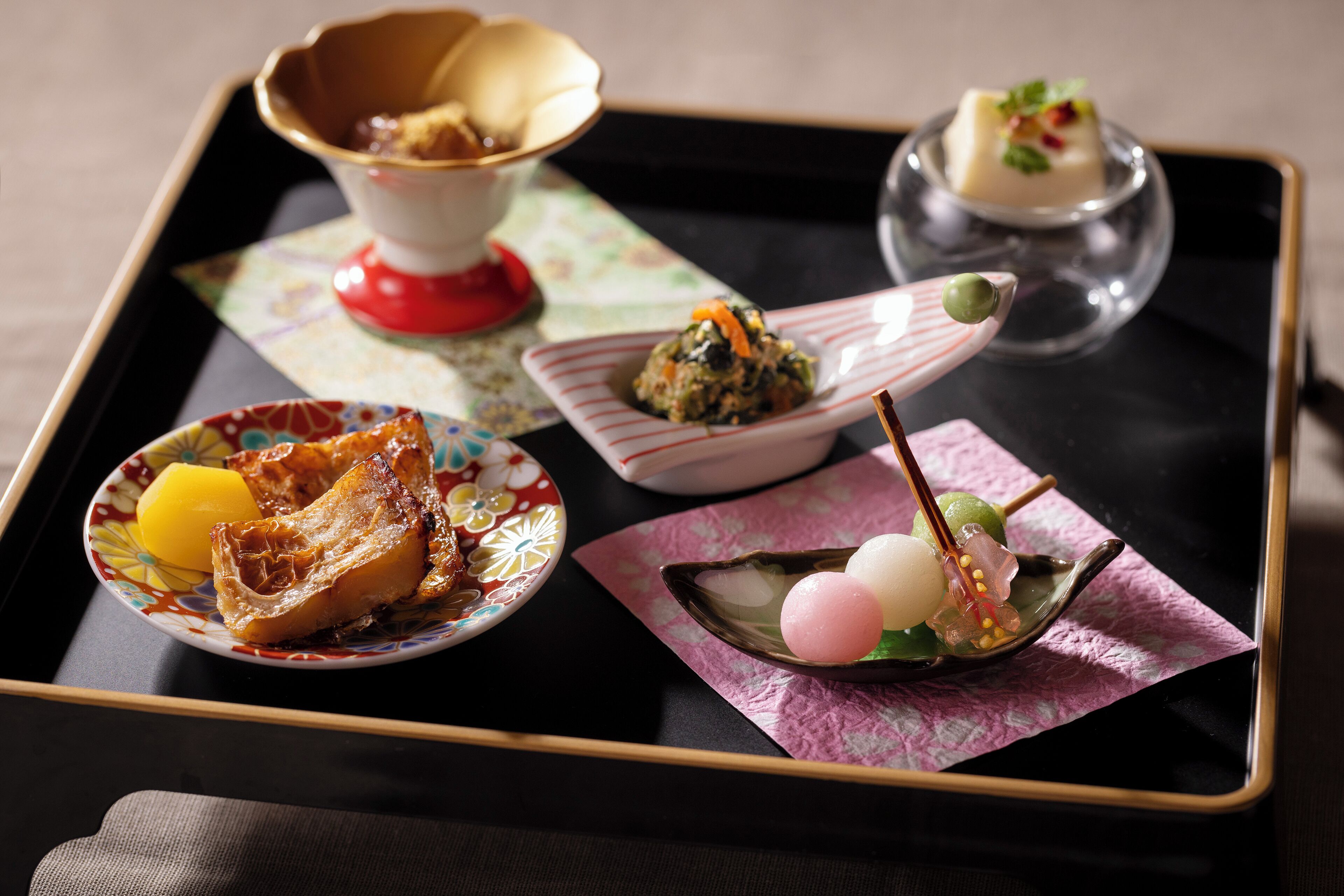 A tray with various Japanese dishes including sushi, a bowl of soup, and a dessert.