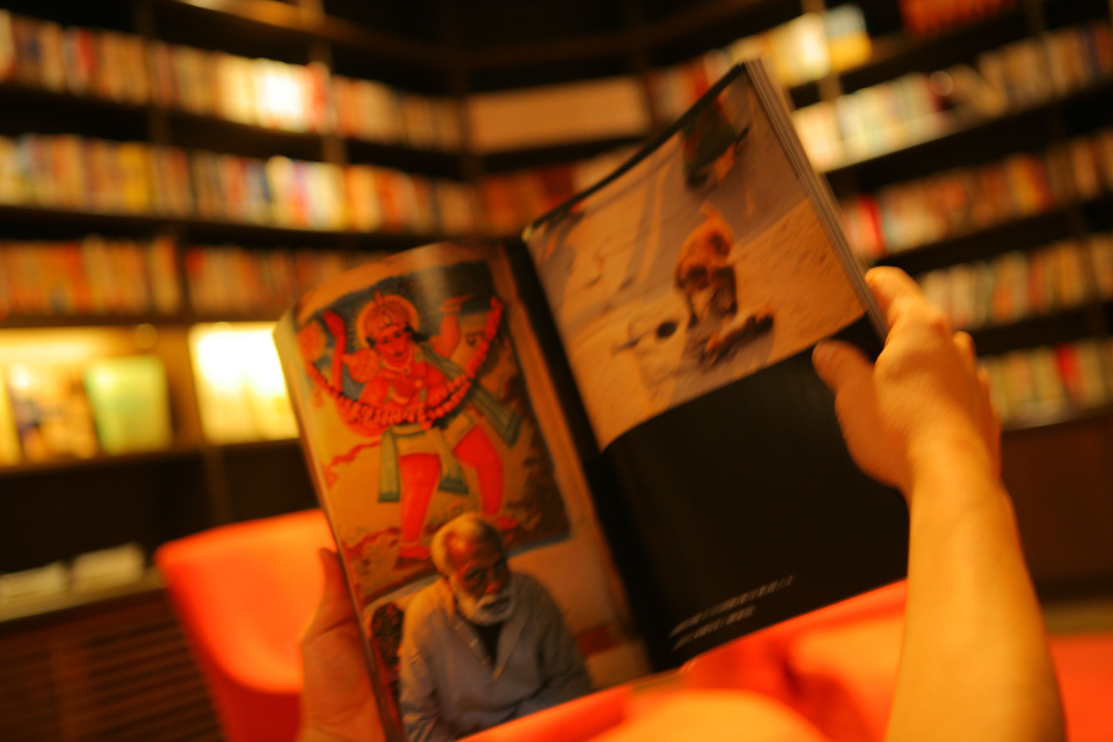 A person reading a book in a library with bookshelves in the background.