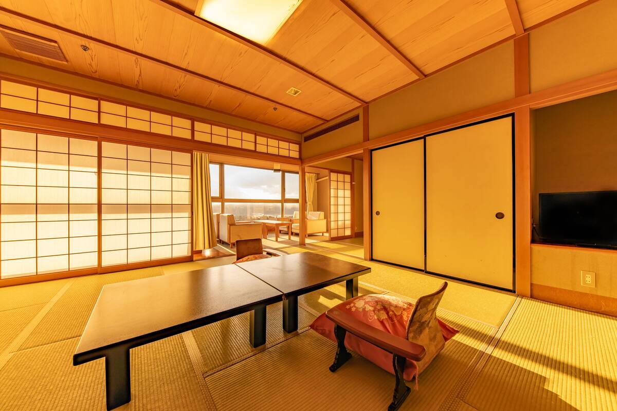 Une pièce de style japonais traditionnel, avec un sol recouvert de tatamis, une table basse, un banc rembourré, des portes coulissantes et un téléviseur.