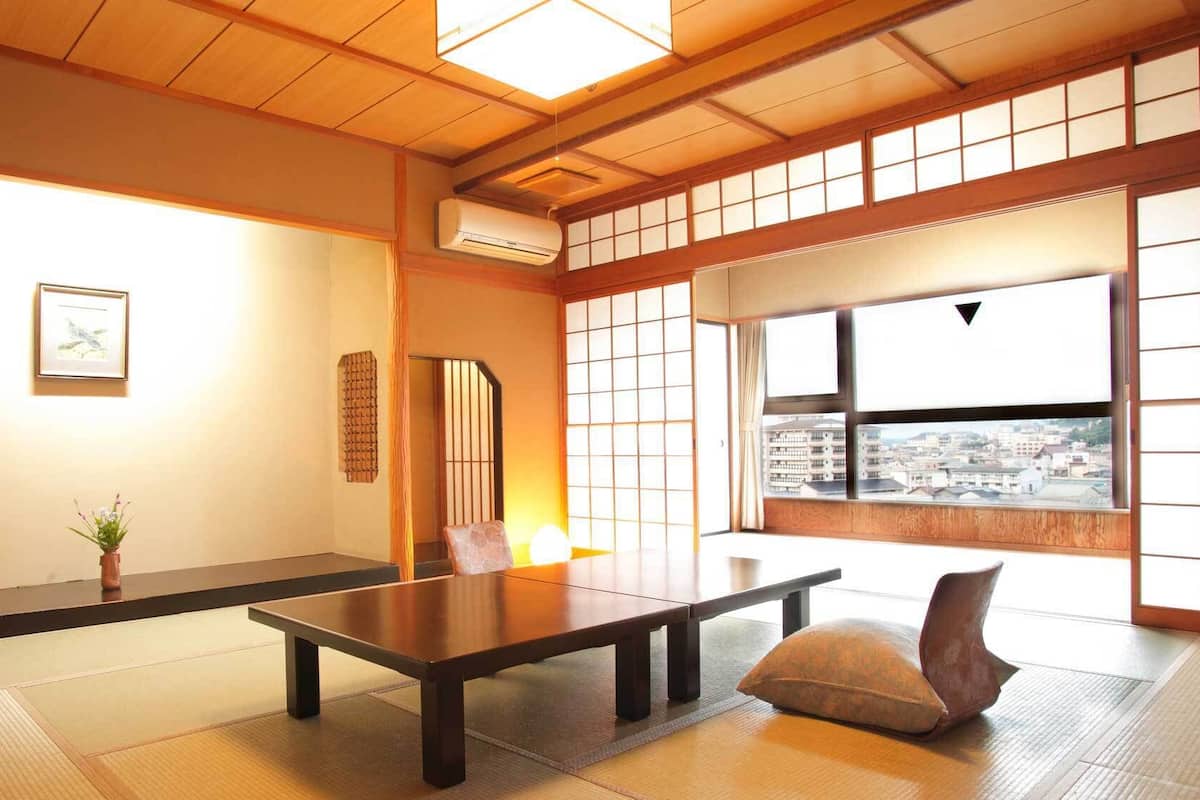 Une pièce de style japonais traditionnel, avec un sol recouvert de tatamis, une table basse, un coussin, un paravent en papier de riz (shoji) et une vue sur la ville.