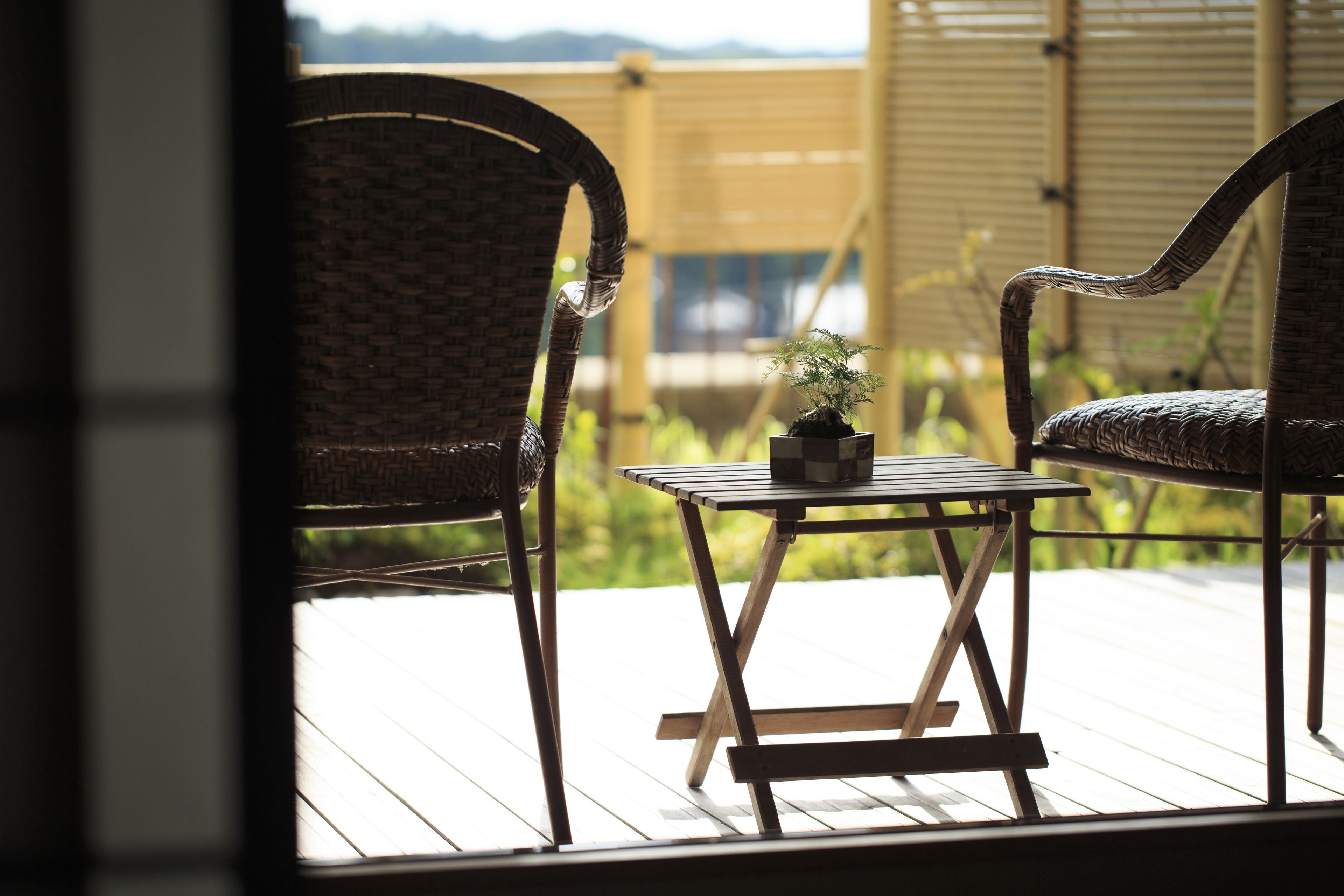 A wicker chair and a small table with a potted plant on a wooden deck.