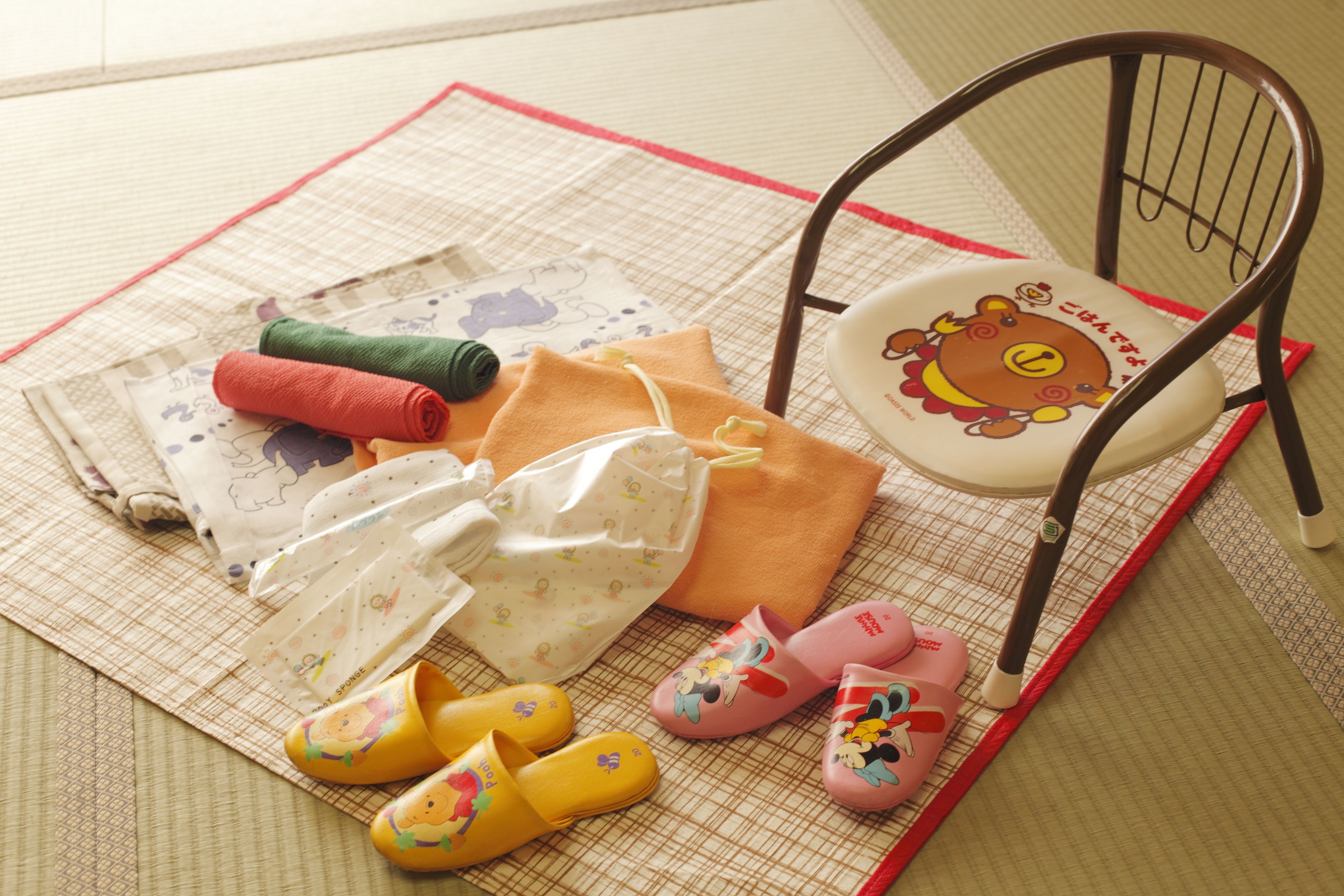 A tatami mat with various children's items including a chair, slippers, and a blanket.