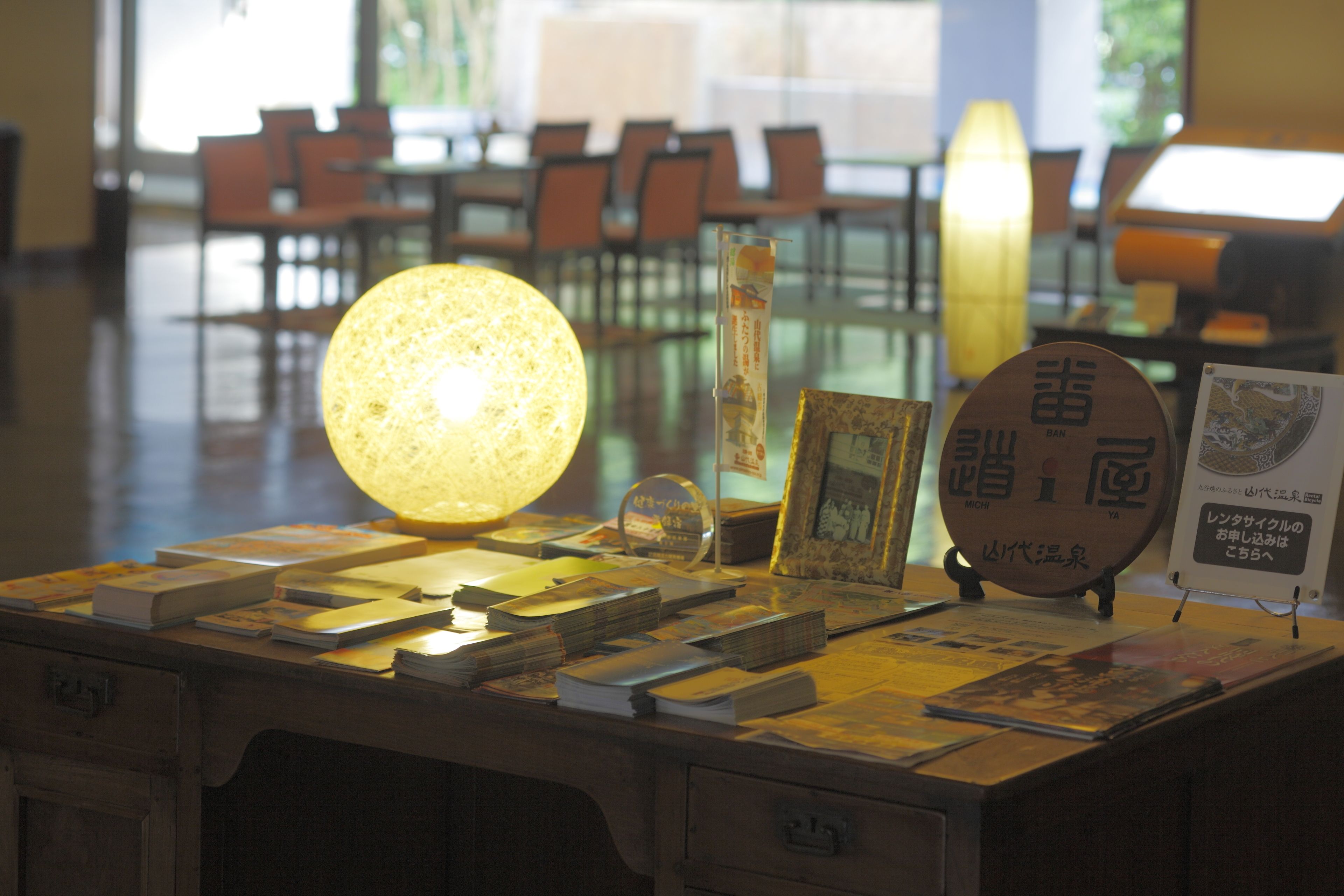 A reception desk with a large spherical lamp, informational posters, and a wooden sign with Japanese characters.