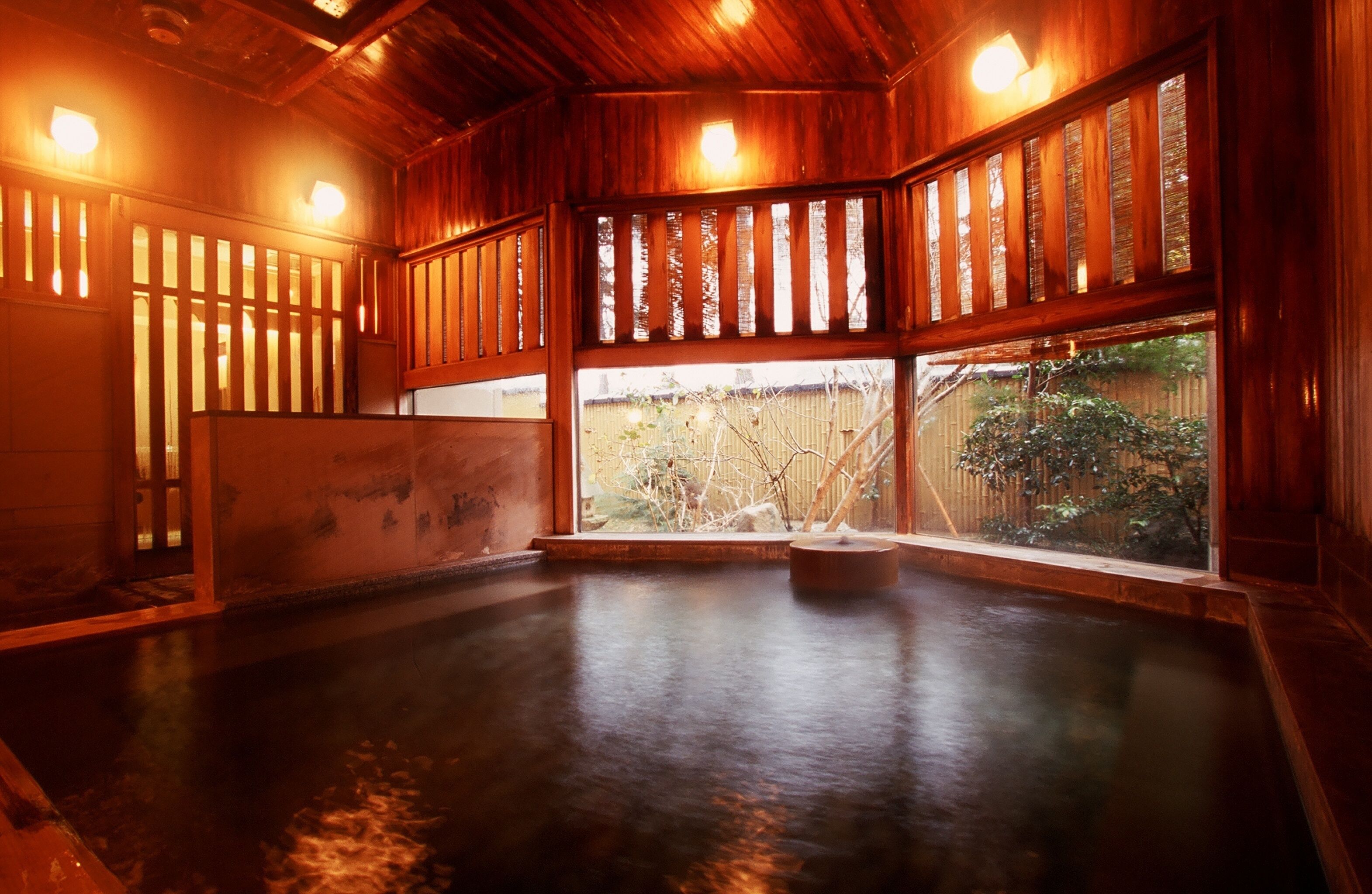 A traditional Japanese onsen with wooden interiors, a stone hot spring, and a view of the surrounding garden.