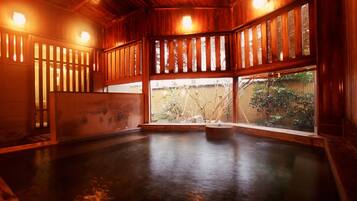 A traditional Japanese onsen with wooden interiors, a stone hot spring, and a view of the surrounding garden.