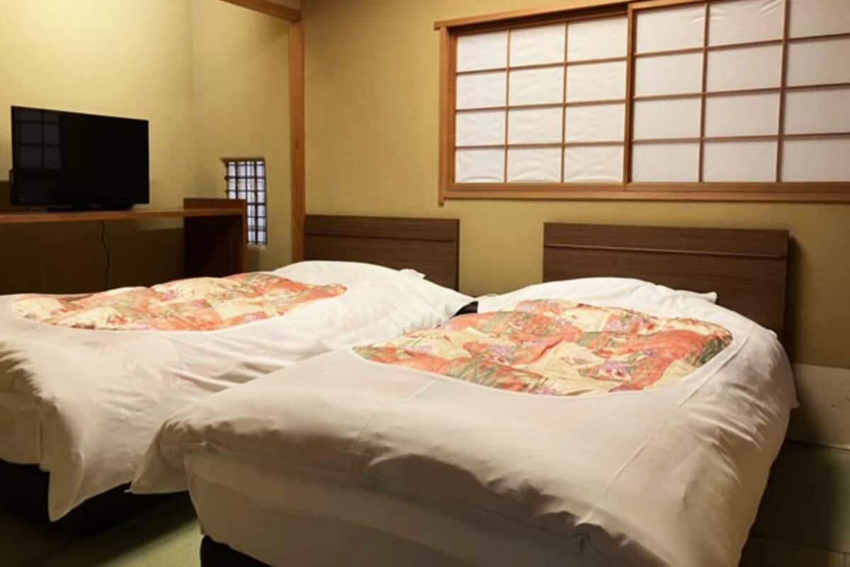 Habitación con dos camas, un televisor y una ventana con diseño de cuadrícula.