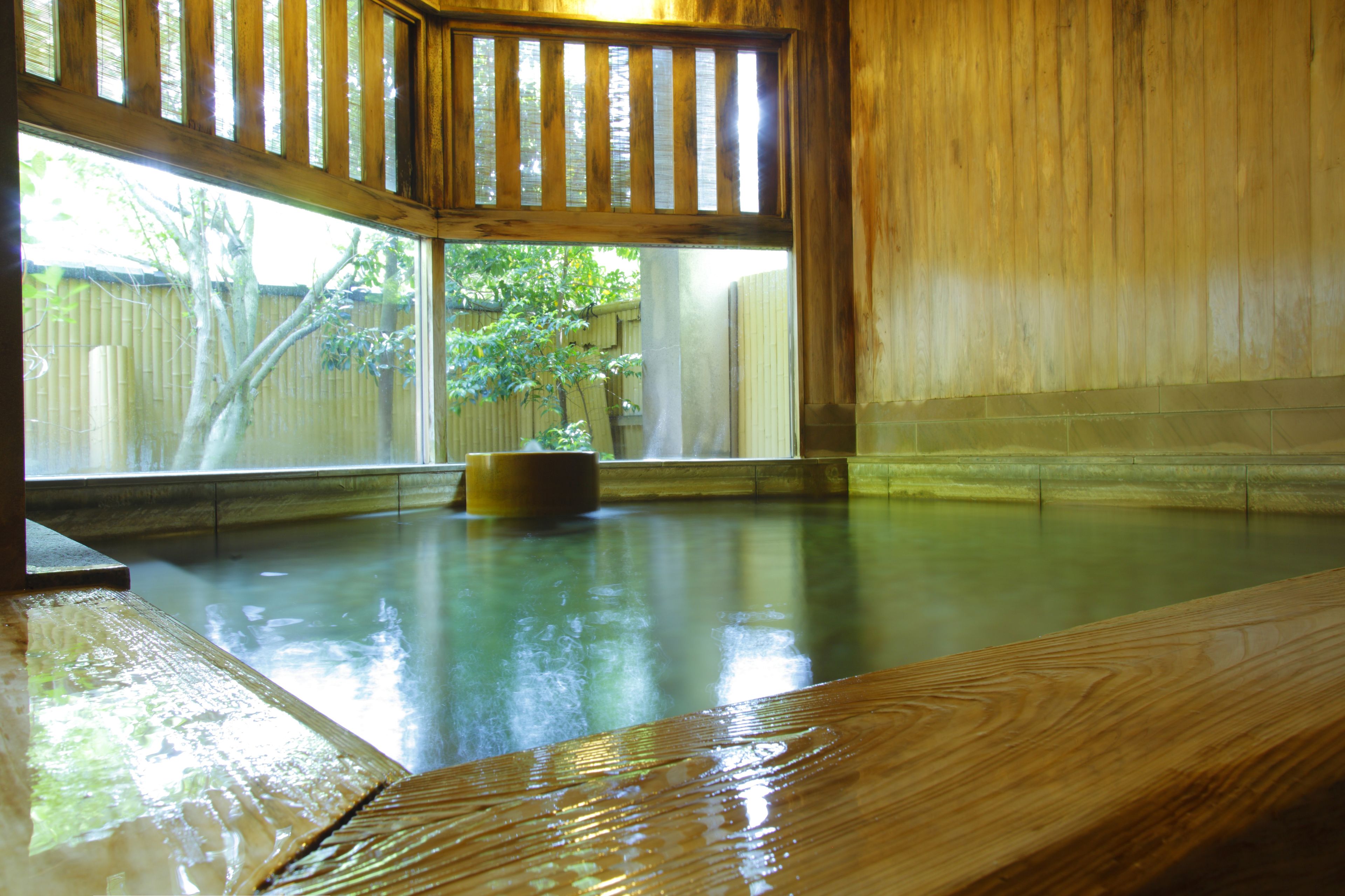 A wooden bath with a view of a bamboo fence and trees outside.