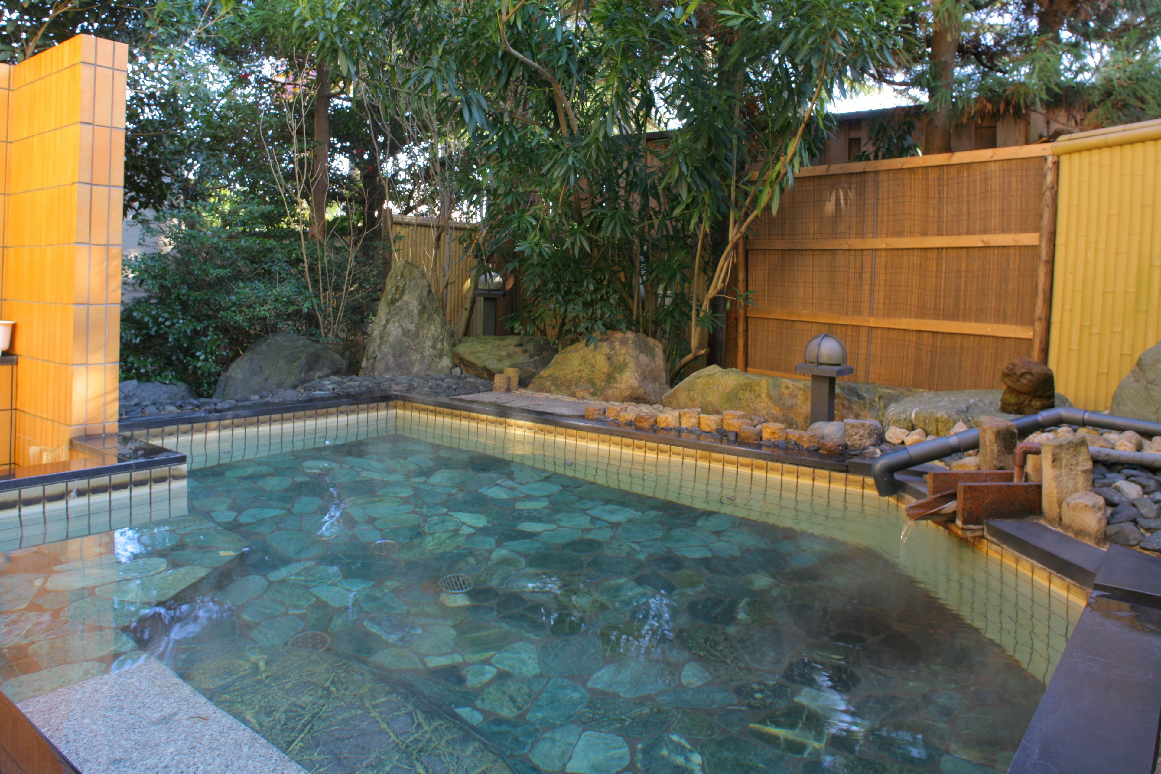A clear pool with rocks and a wooden fence in the background.