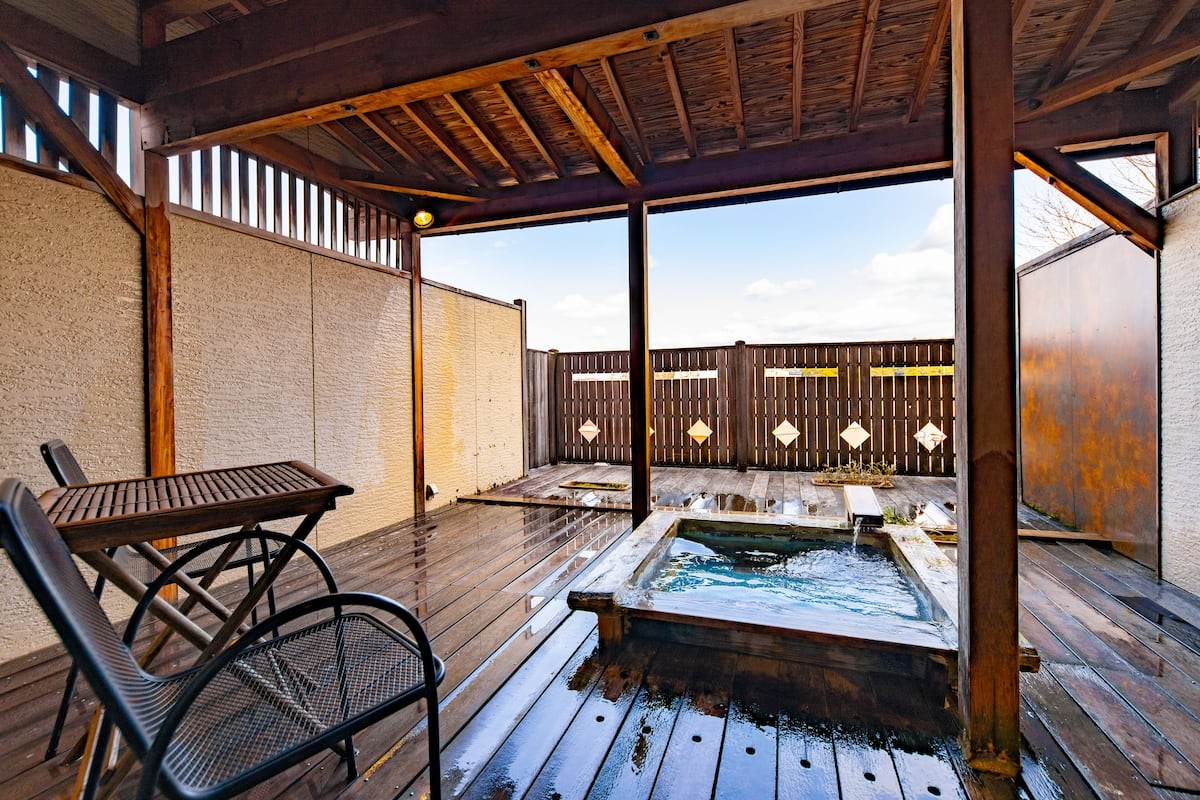 Une terrasse en bois avec un jacuzzi, une table et des chaises.