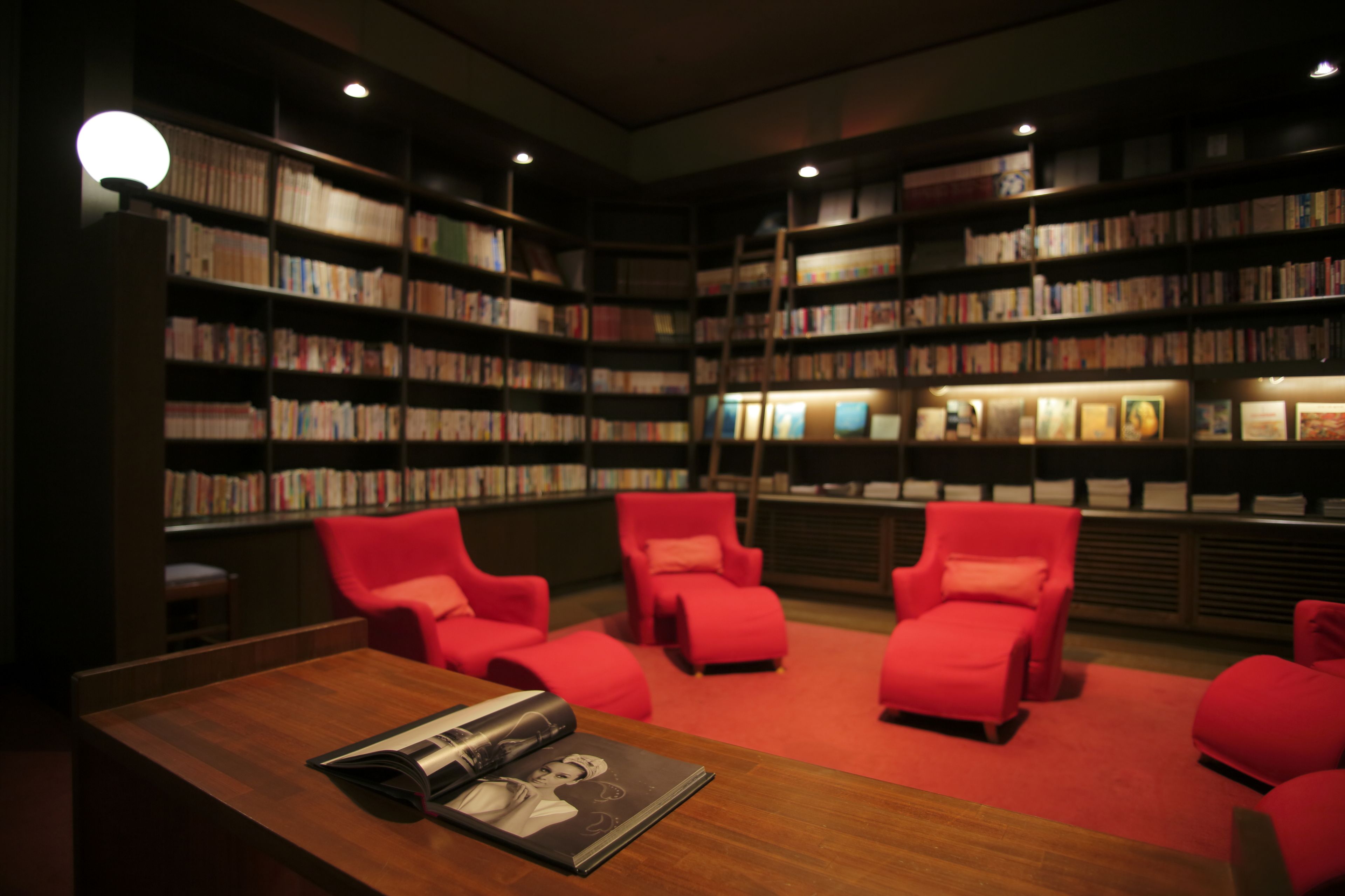 A library with bookshelves, red chairs, and a wooden table with a magazine.