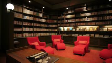 A library with bookshelves, red chairs, and a wooden table with a magazine.