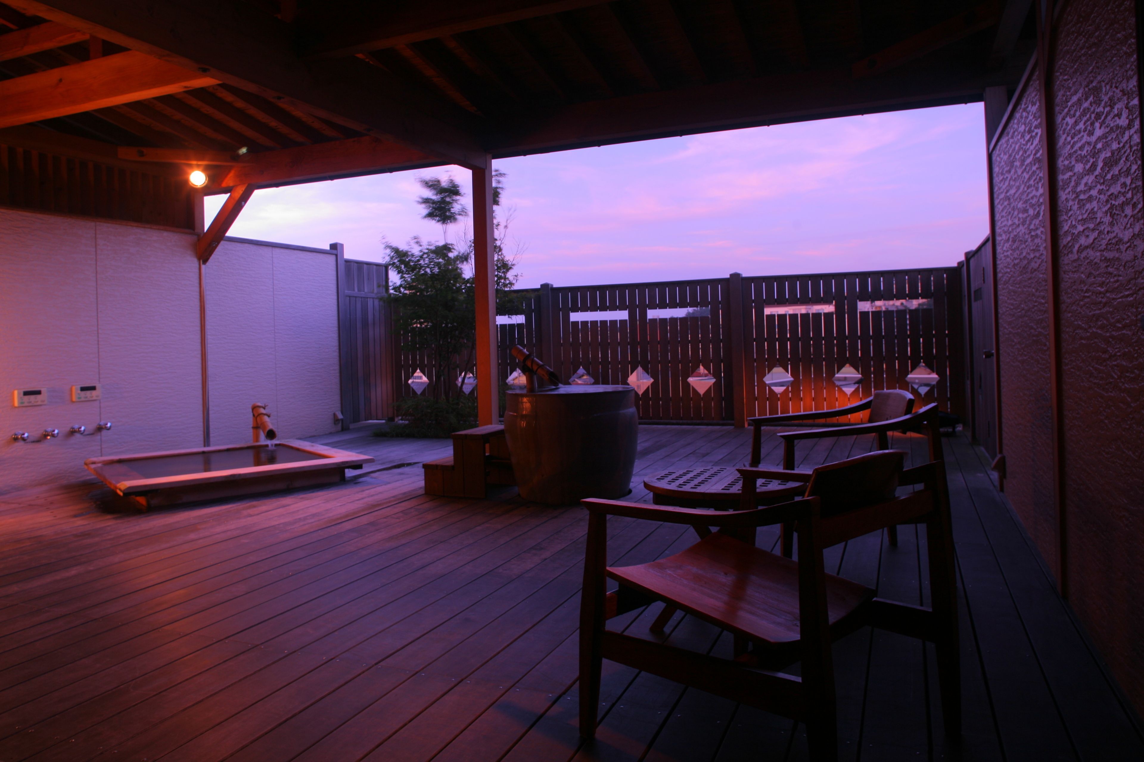 An outdoor patio with wooden flooring, a seating area with chairs, a table, and a large barrel.