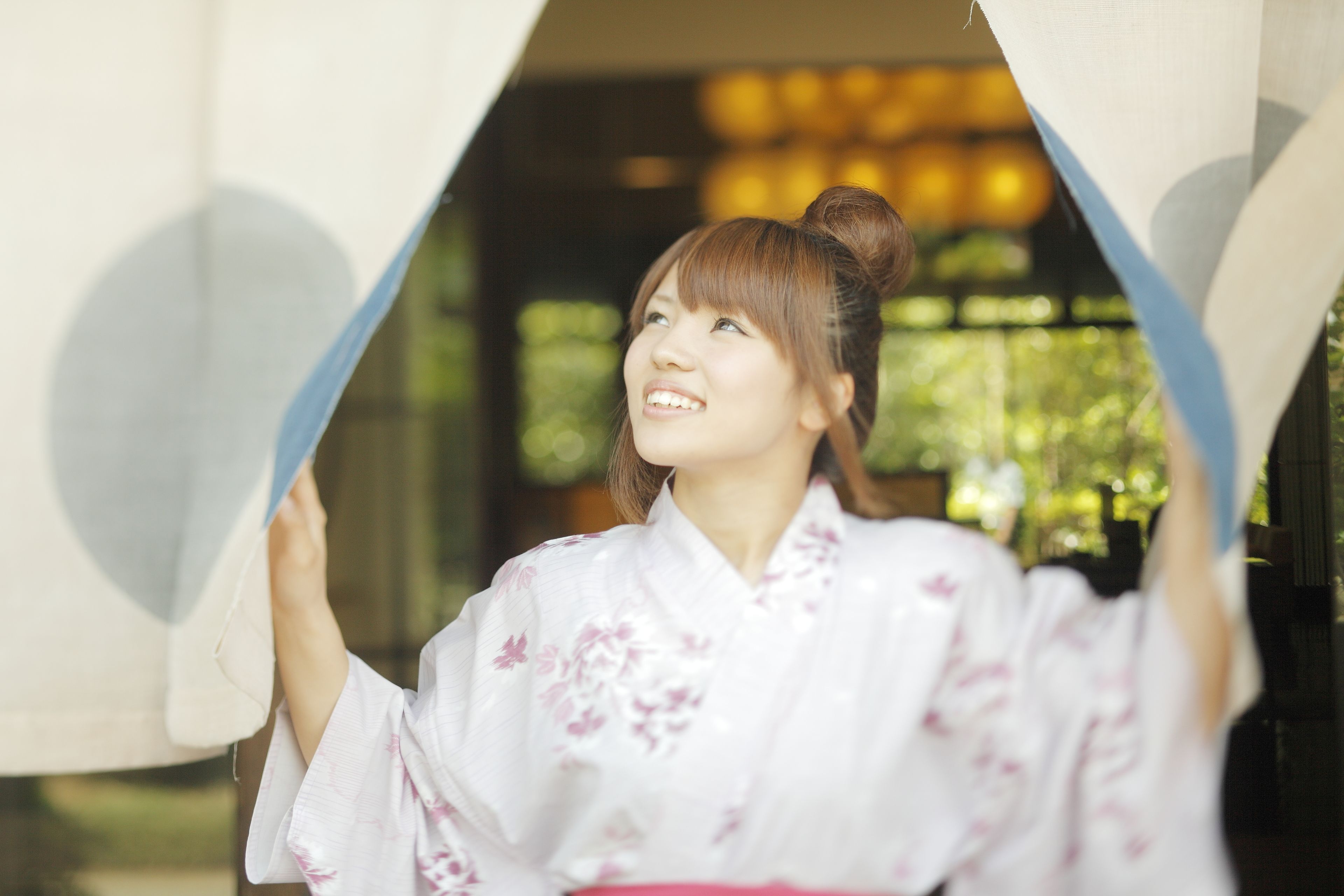 A person in a traditional white kimono with floral patterns, standing in a doorway with a curtain.