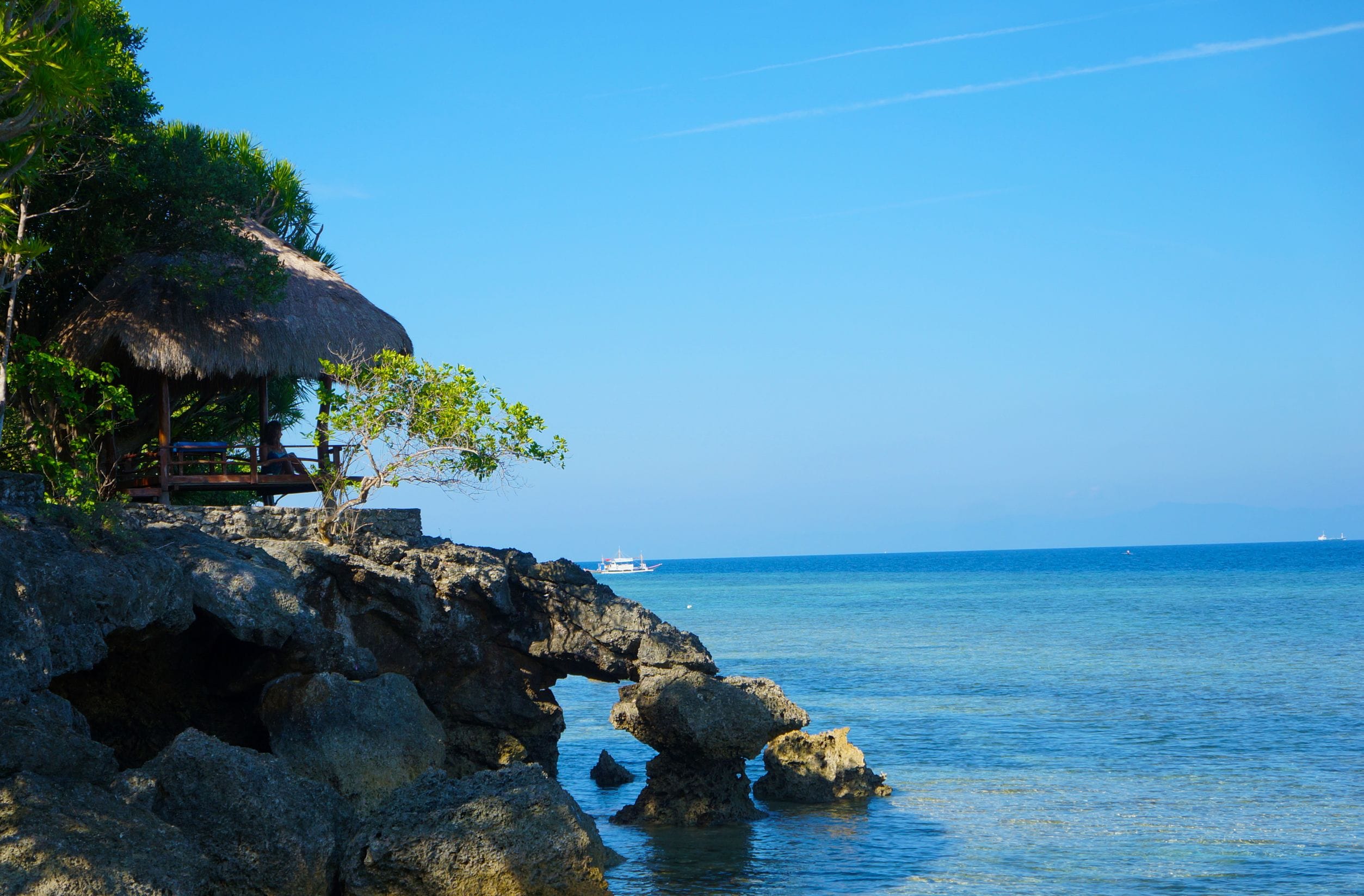 A rocky shoreline with a thatched-roof structure and a clear view of the ocean.