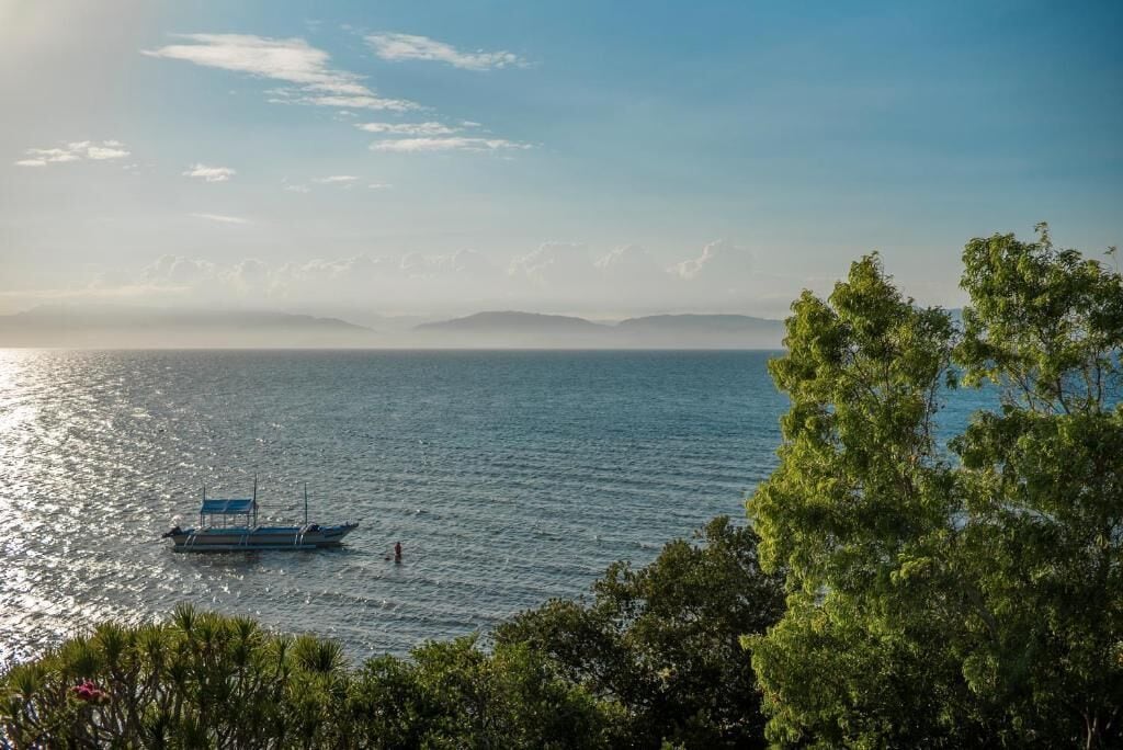 A calm sea with a boat and distant mountains under a clear sky.