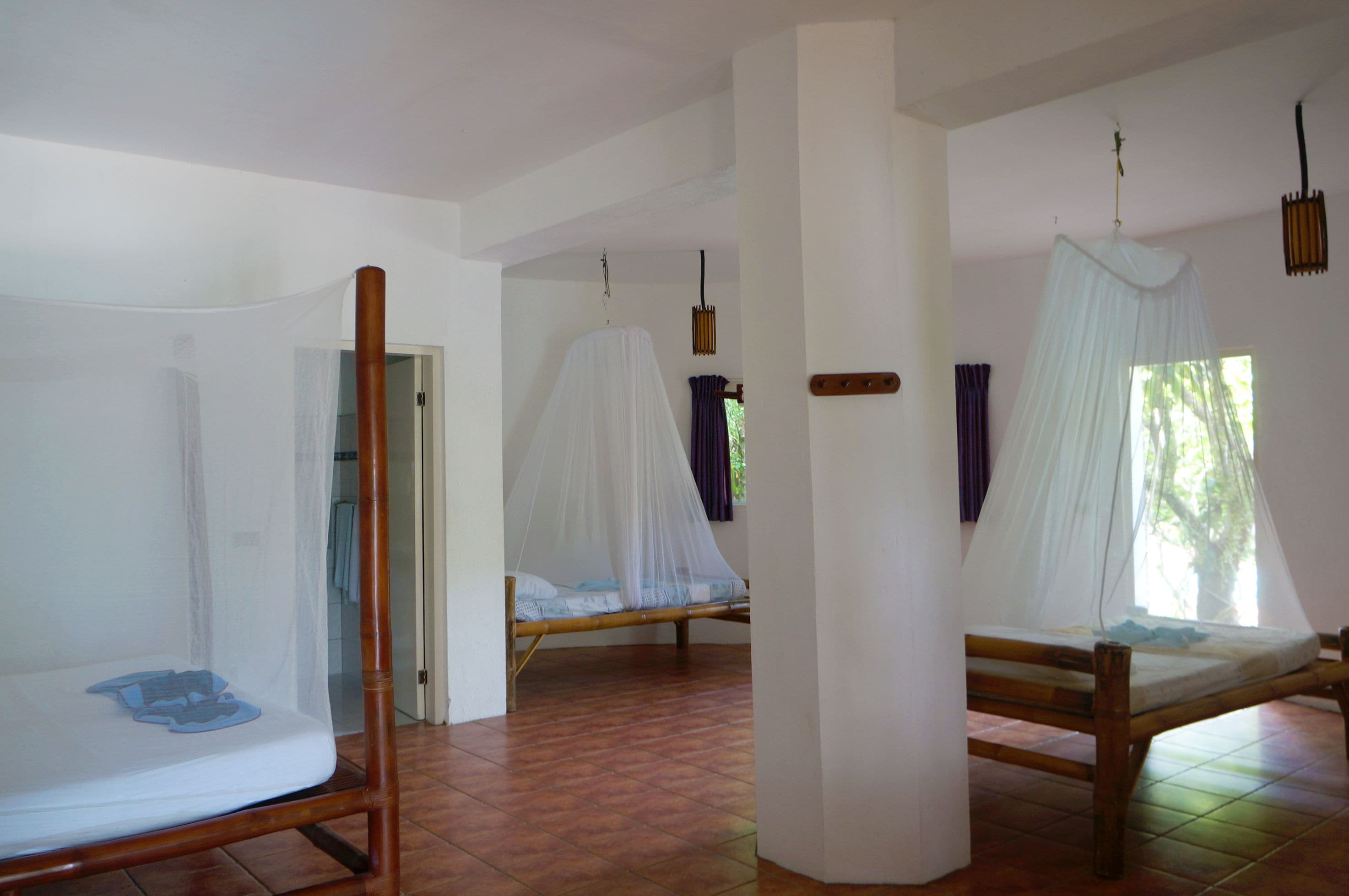 Een kamer met twee bedden, elk voorzien van een klamboe, houten frames en een witte matras.