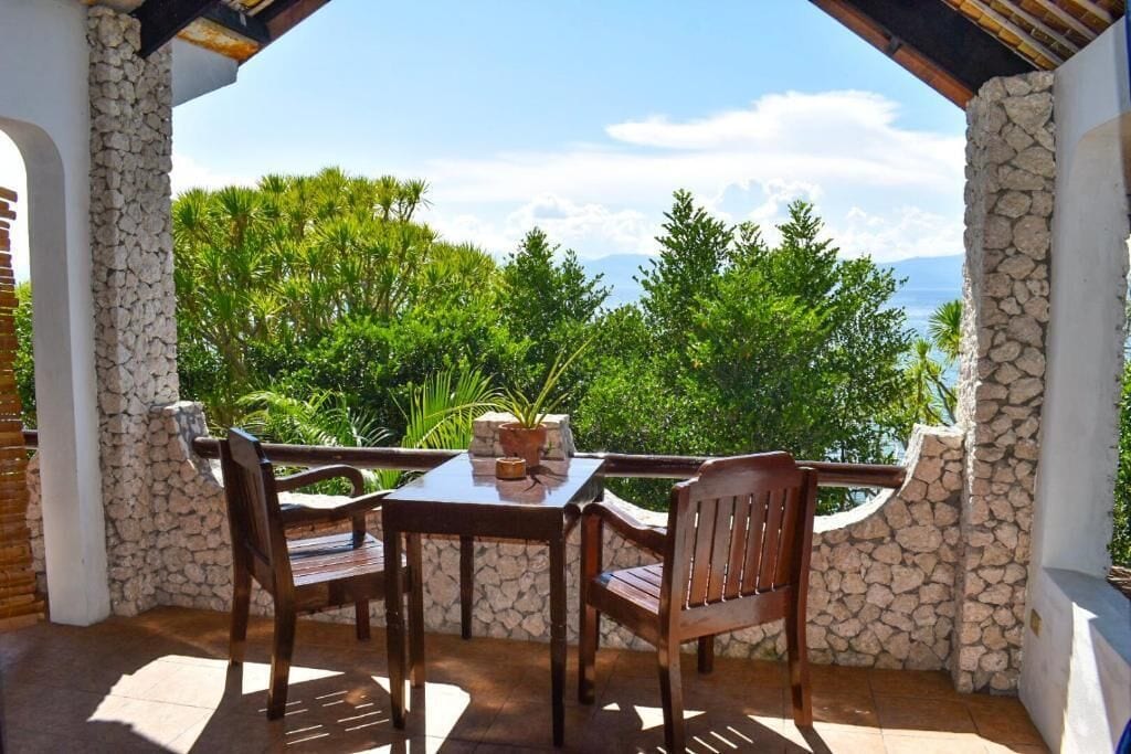 A covered outdoor seating area with a stone wall, a table, and two chairs.