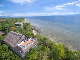 Una casa con techo de paja y un balcón con vistas a una playa y aguas cristalinas.