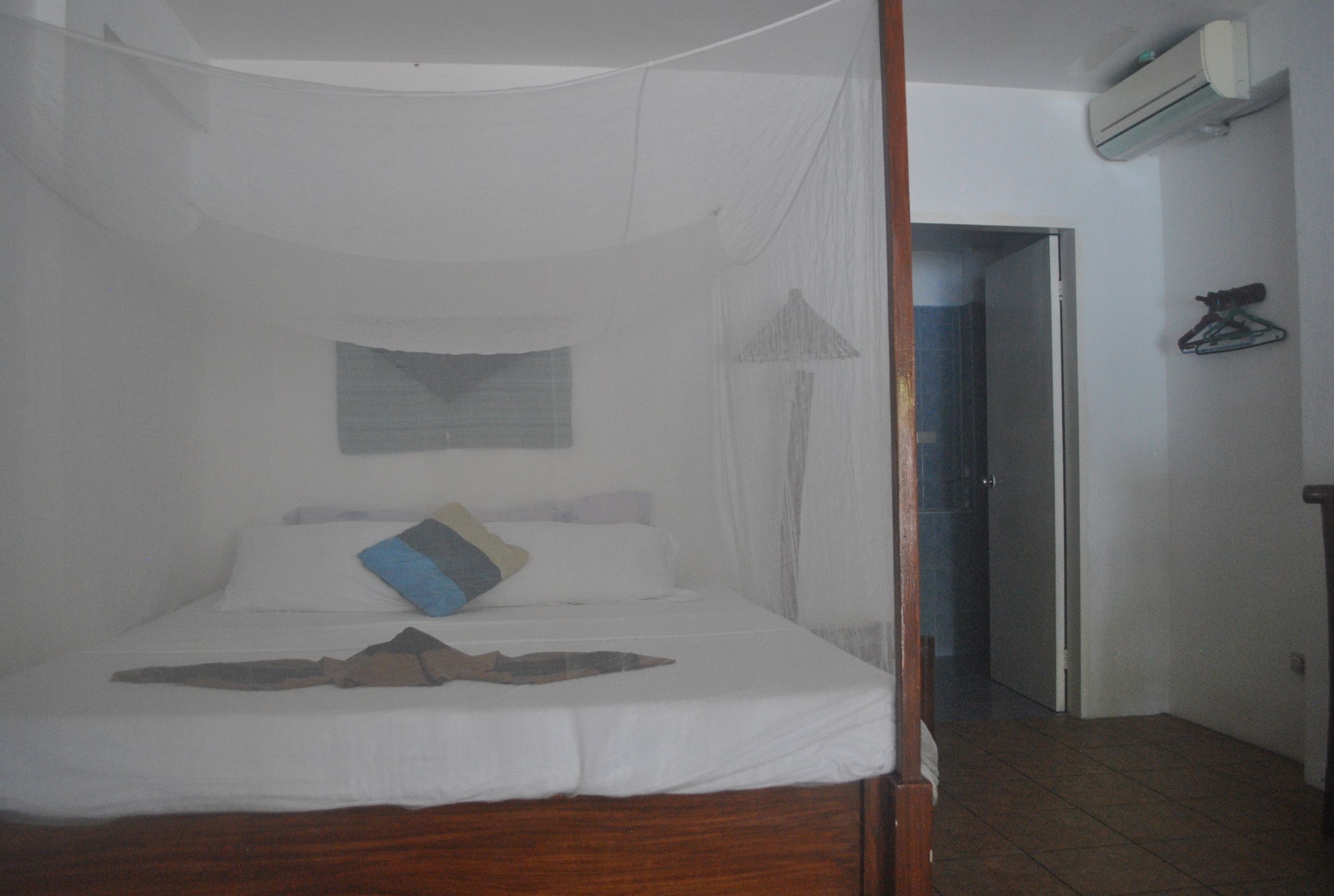 A bed with a canopy, a wall-mounted air conditioner, and a door leading to another room.