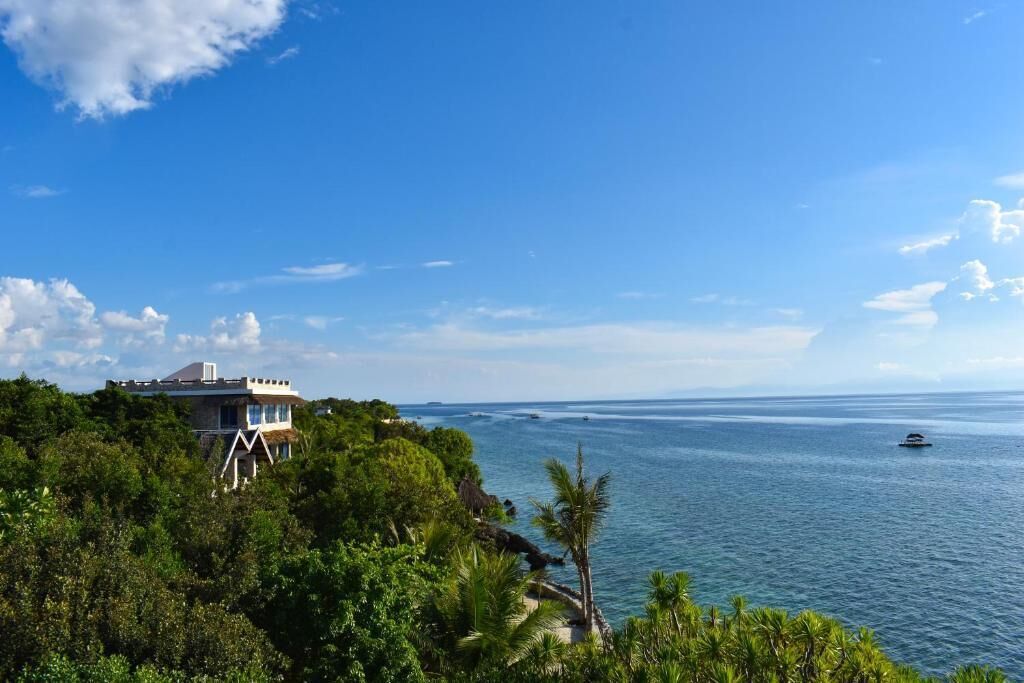 A coastal property with a large house overlooking the sea, surrounded by lush greenery.