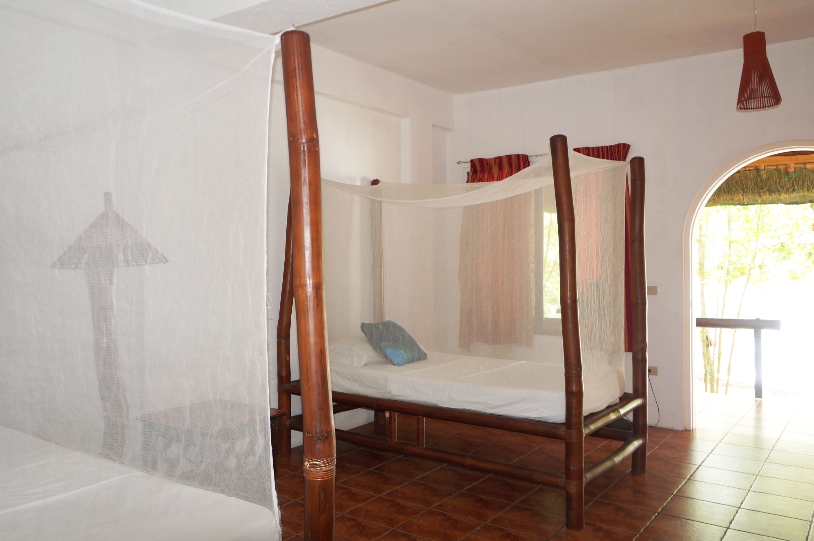 A room with a four-poster bed, a mosquito net, and a view of the outdoors.
