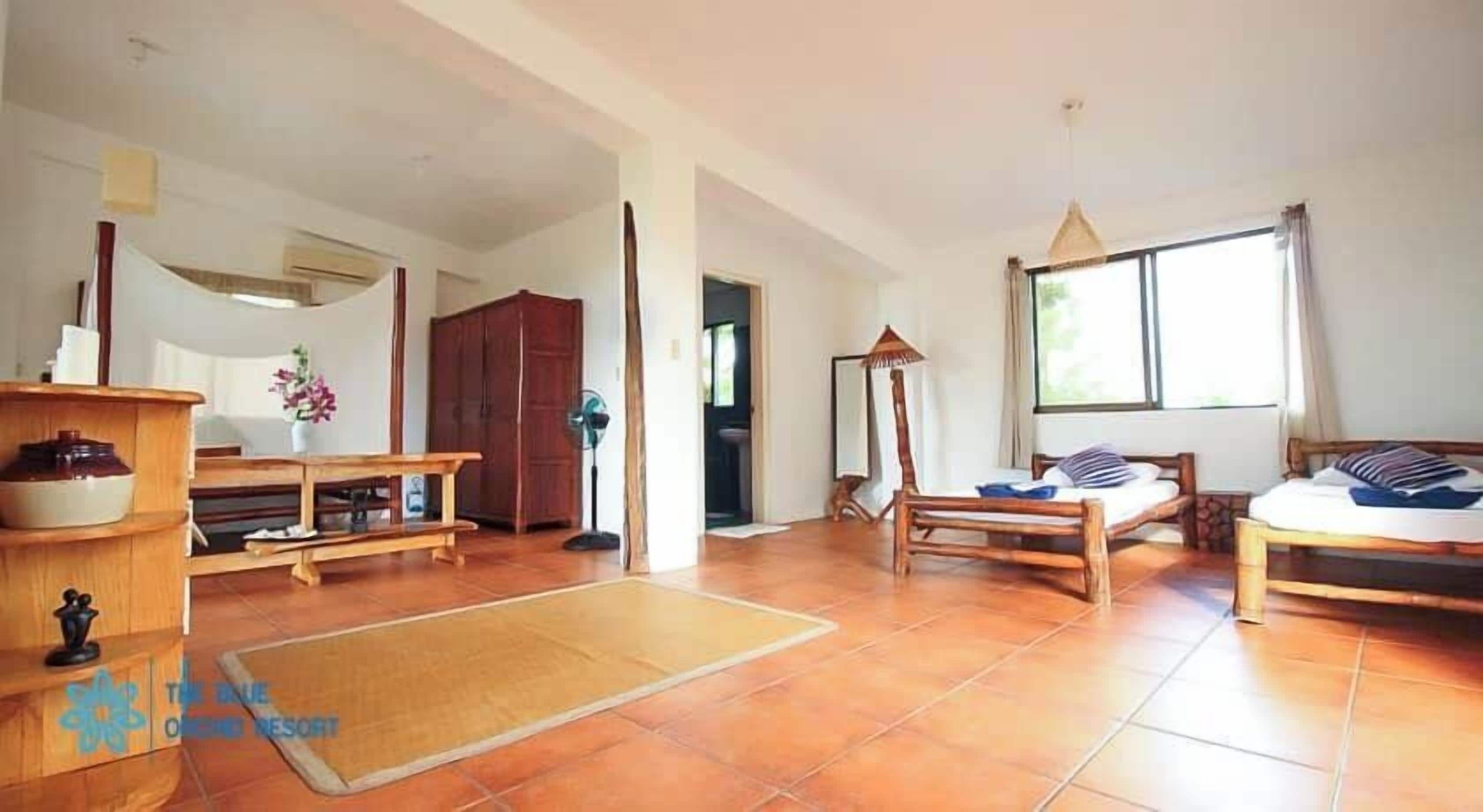 Ein geräumiger Wohnbereich mit einem Holzsofa, einem Holztisch und einem Bett mit Holzrahmen. Ein großes Fenster sorgt für natürliches Licht.