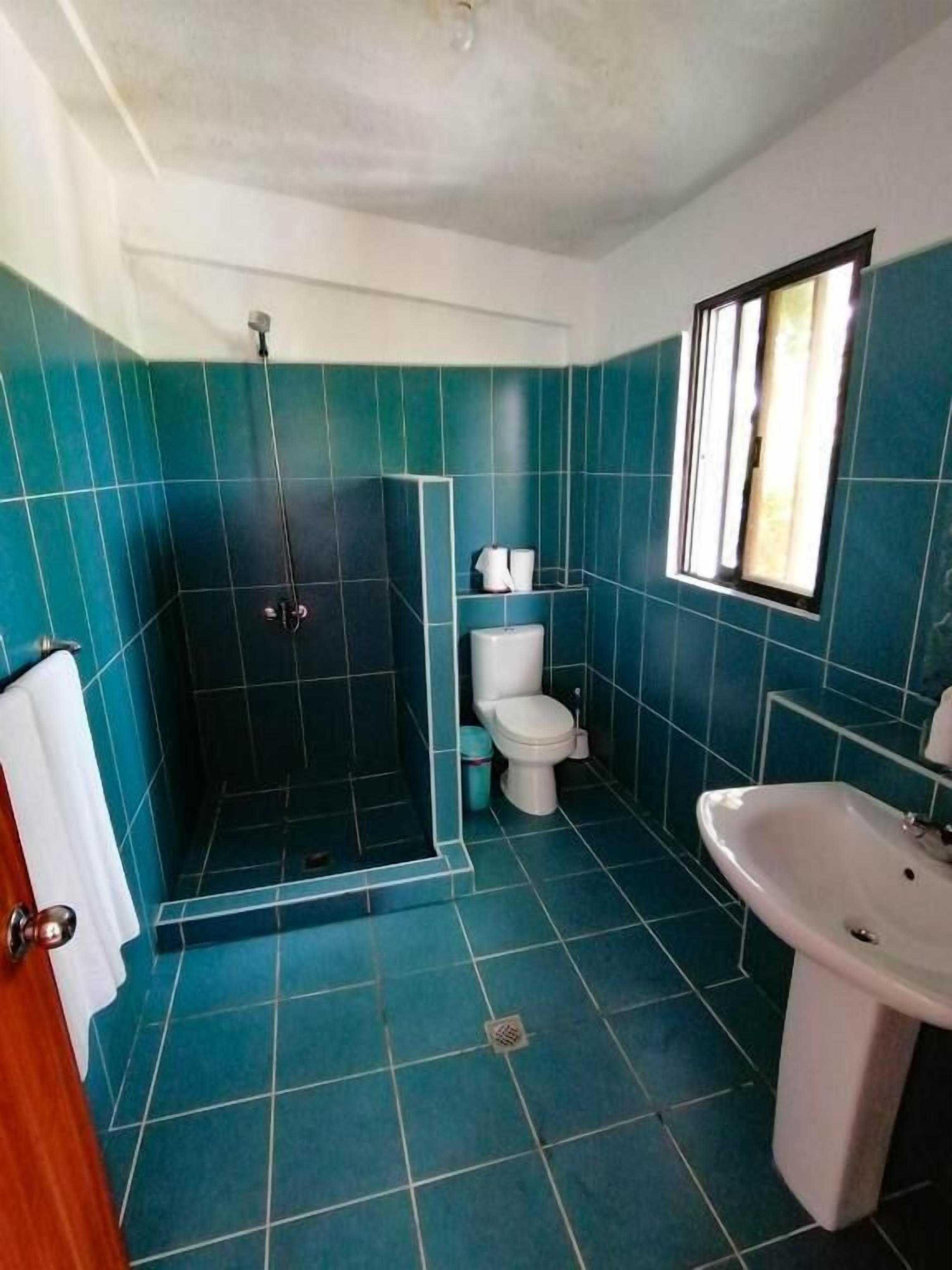 A bathroom with teal tiles, a white toilet, a shower enclosure, and a sink.