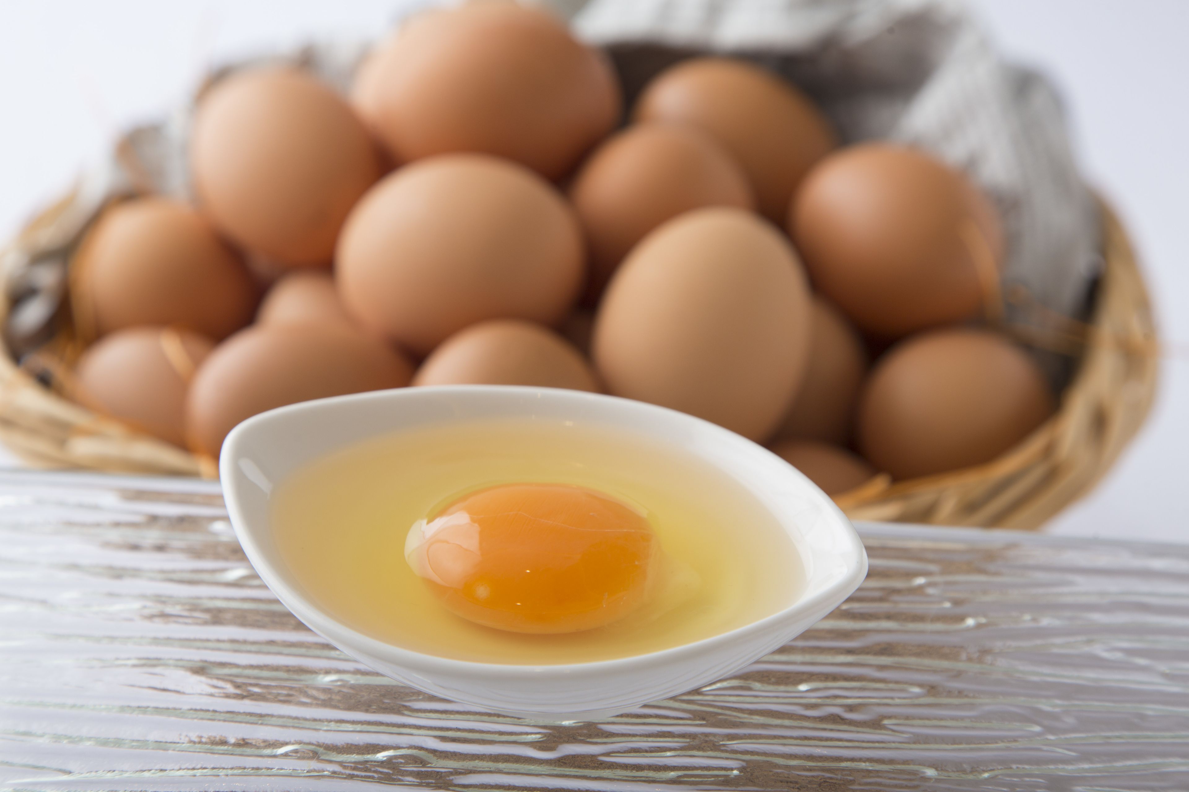 A bowl of egg yolk with a basket of eggs in the background.
