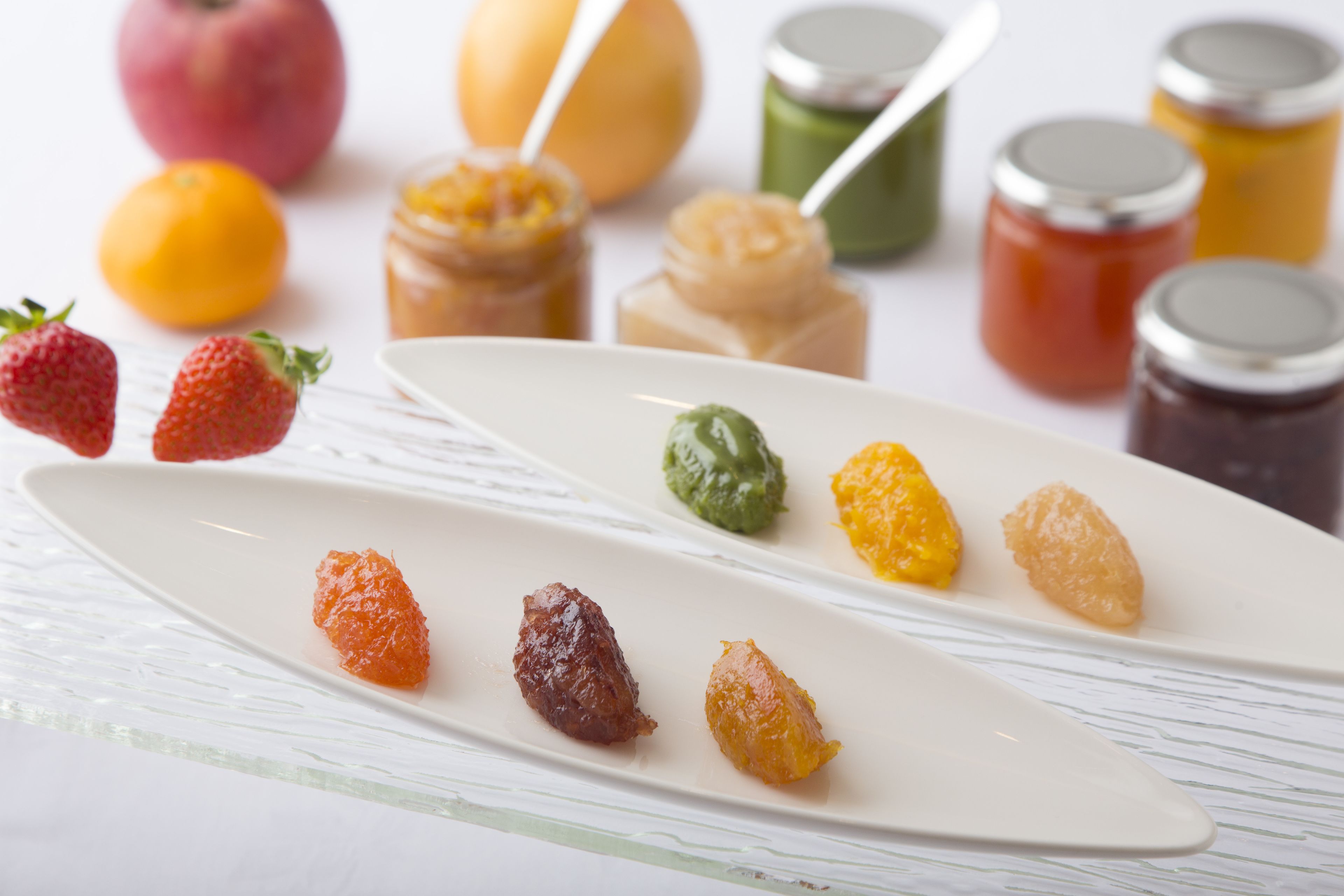 Un piatto bianco con diversi frutti conservati e barattoli di marmellata.