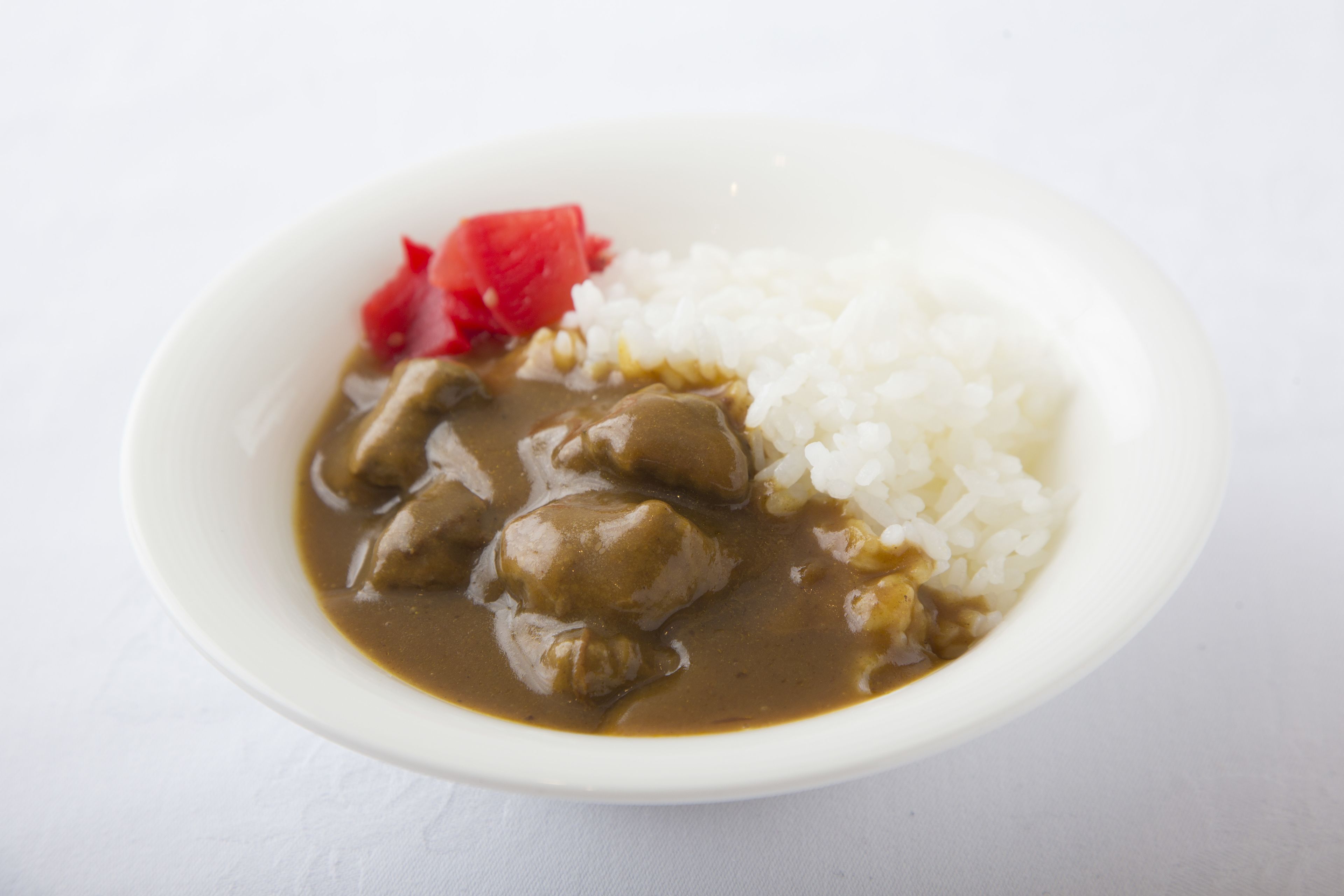 Eine Schüssel mit Essen, darunter Reis, eine braune Soße, möglicherweise mit Fleisch, sowie eine Scheibe roter Frucht.