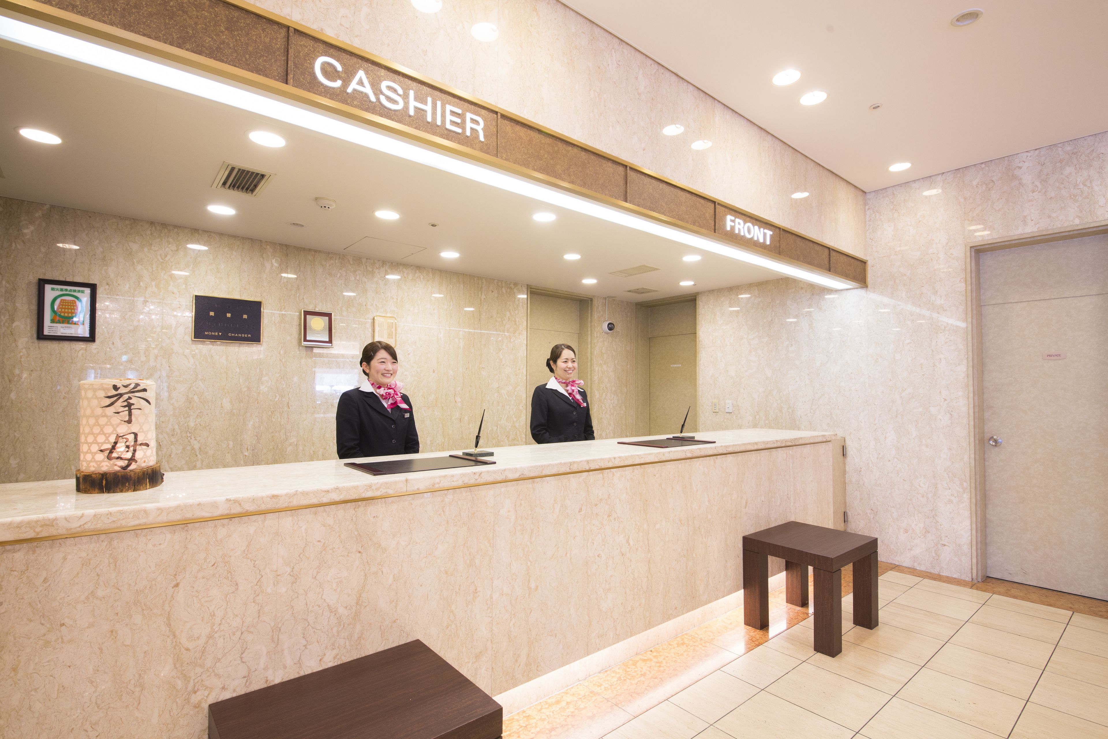 A hotel reception area with a marble counter, two receptionists, and a sign indicating the front desk.