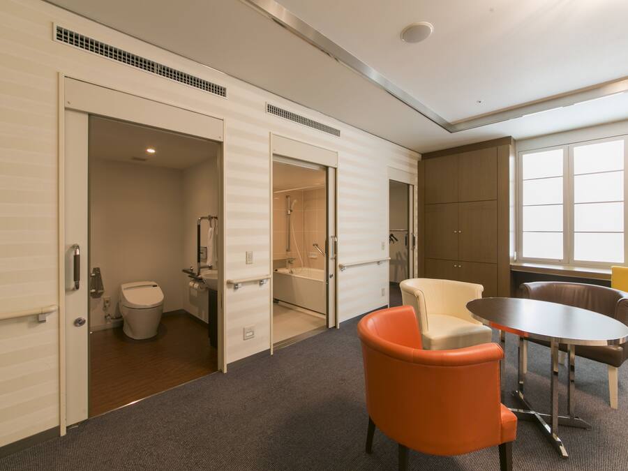 A hotel room with a bathroom, a table, and two chairs.