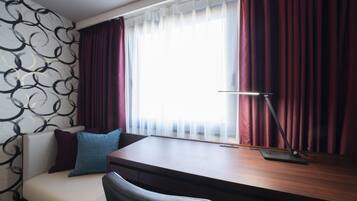 A room with a desk, a chair, a window with curtains, and a wall with a black and white pattern.