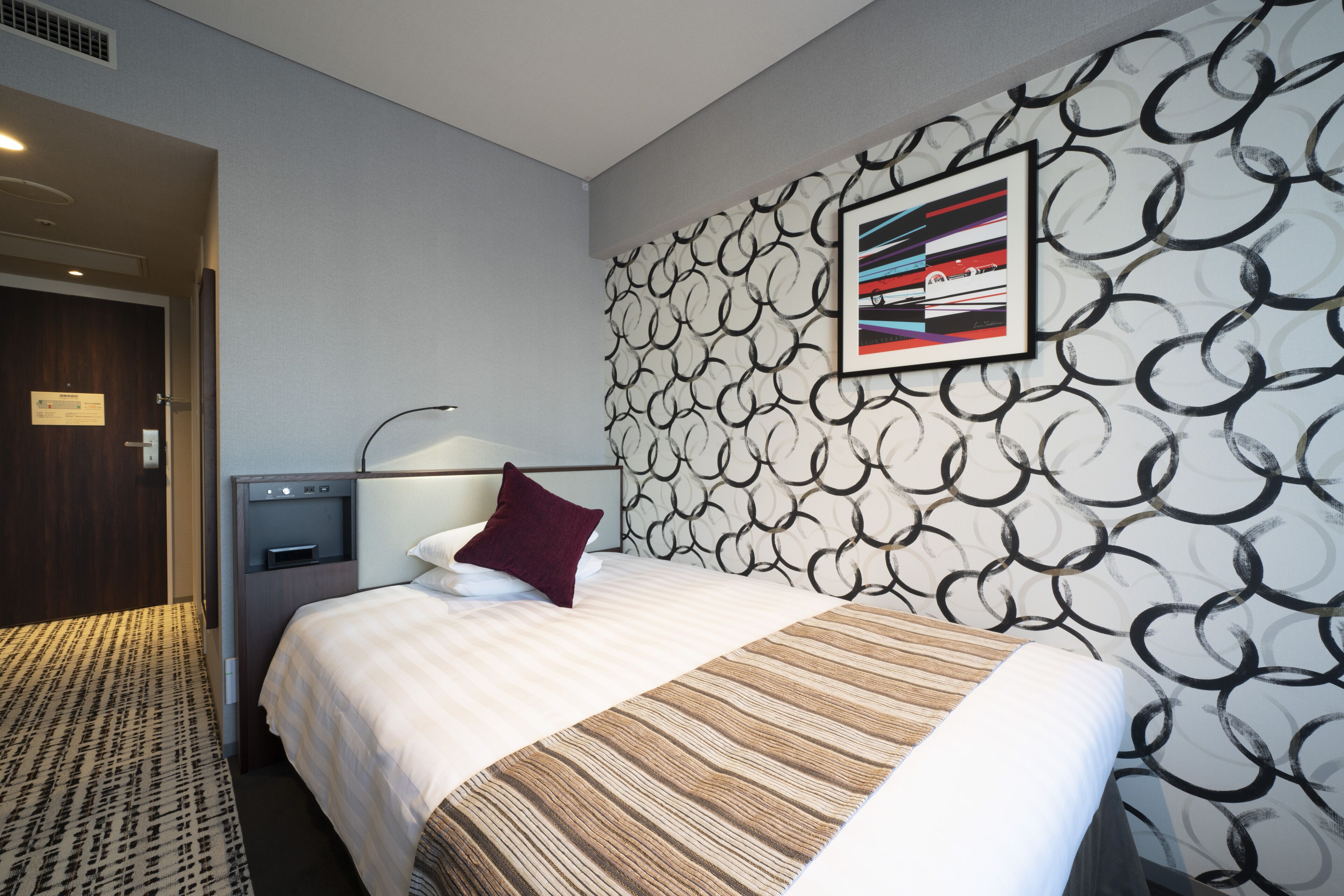 Una camera d'albergo con un letto, una testiera, un'opera d'arte appesa al muro e un tappeto decorato.