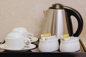 Una bandeja con una cafetera de acero inoxidable, tazas y platillos blancos, y un recipiente con bolsitas de té.