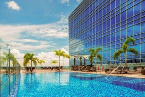 A swimming pool with lounge chairs and palm trees, adjacent to a modern glass building. - Richmonde Hotel Iloilo (Iloilo)