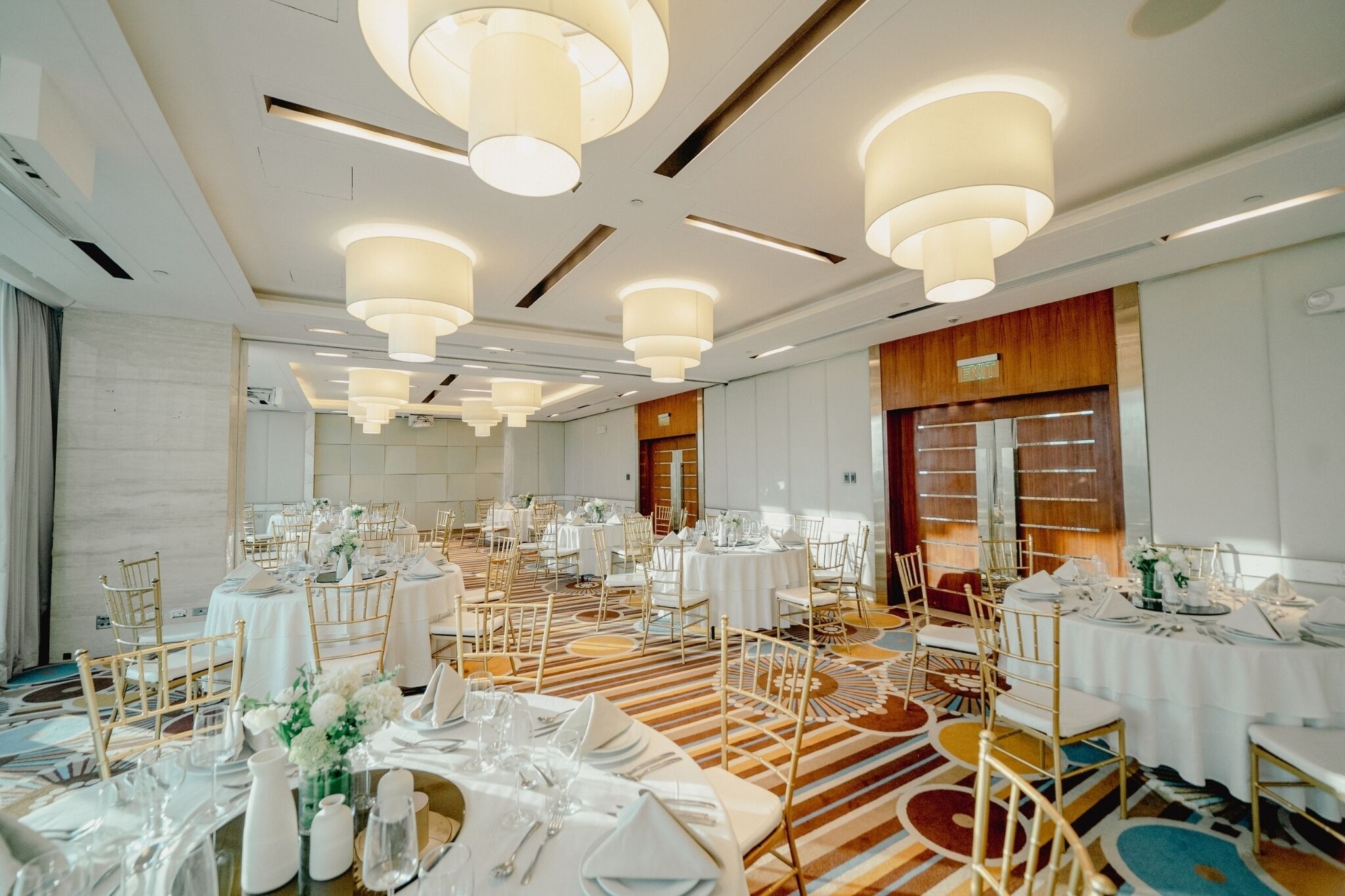 A banquet hall with round tables, white tablecloths, and gold chairs.