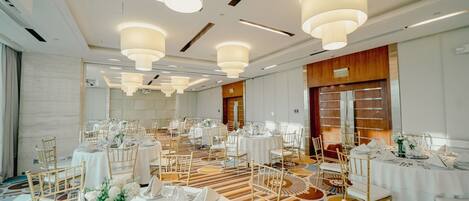 A banquet hall with round tables, white tablecloths, and gold chairs.