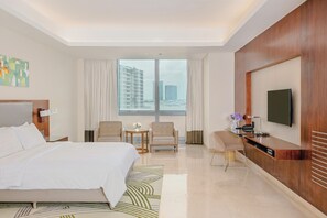 A hotel room with a large bed, a desk, two chairs, a TV, and a view of buildings. - Richmonde Hotel Iloilo (Iloilo)