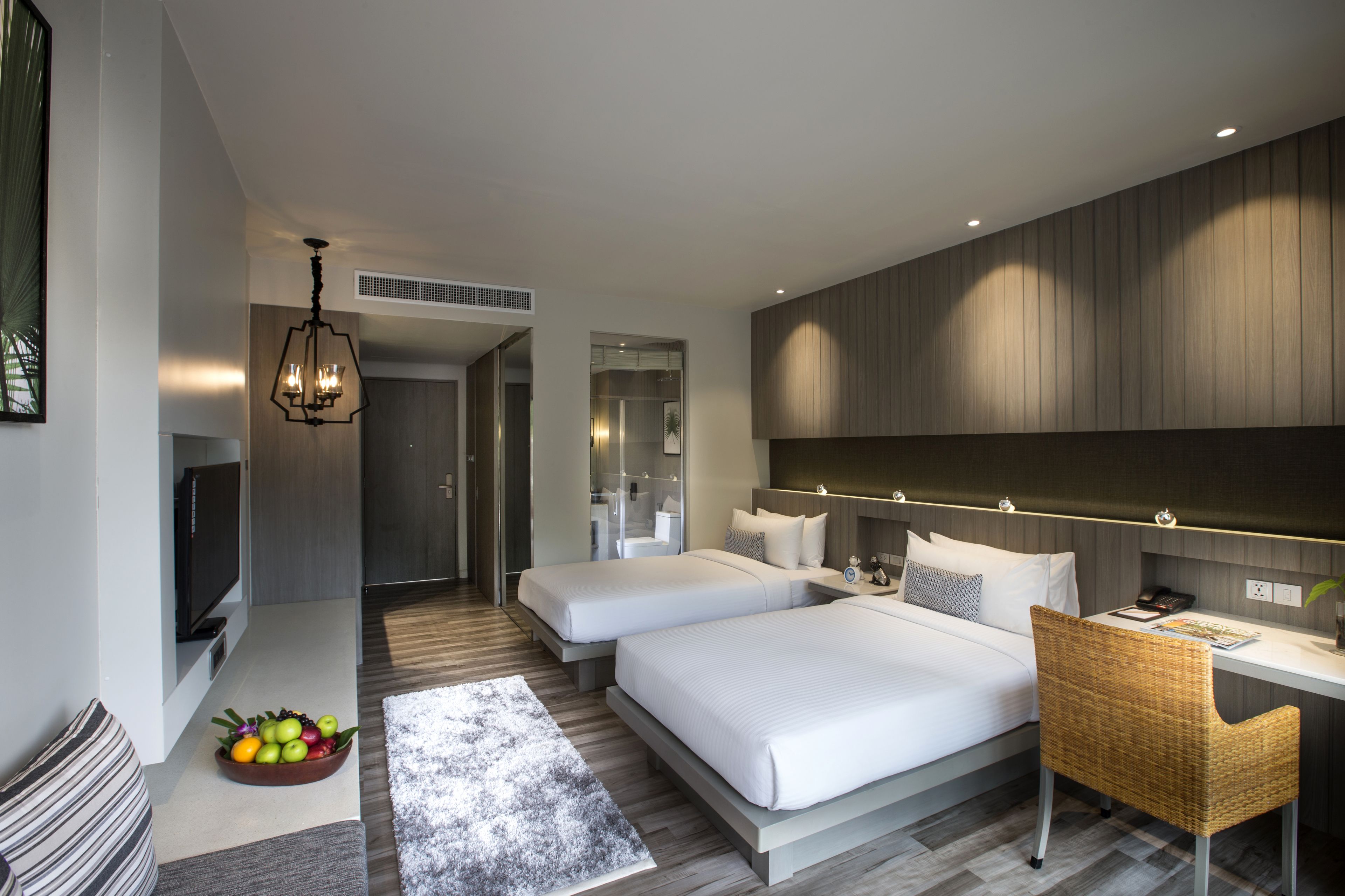 Una habitación de hotel moderna con dos camas, un escritorio, un televisor y un frutero.