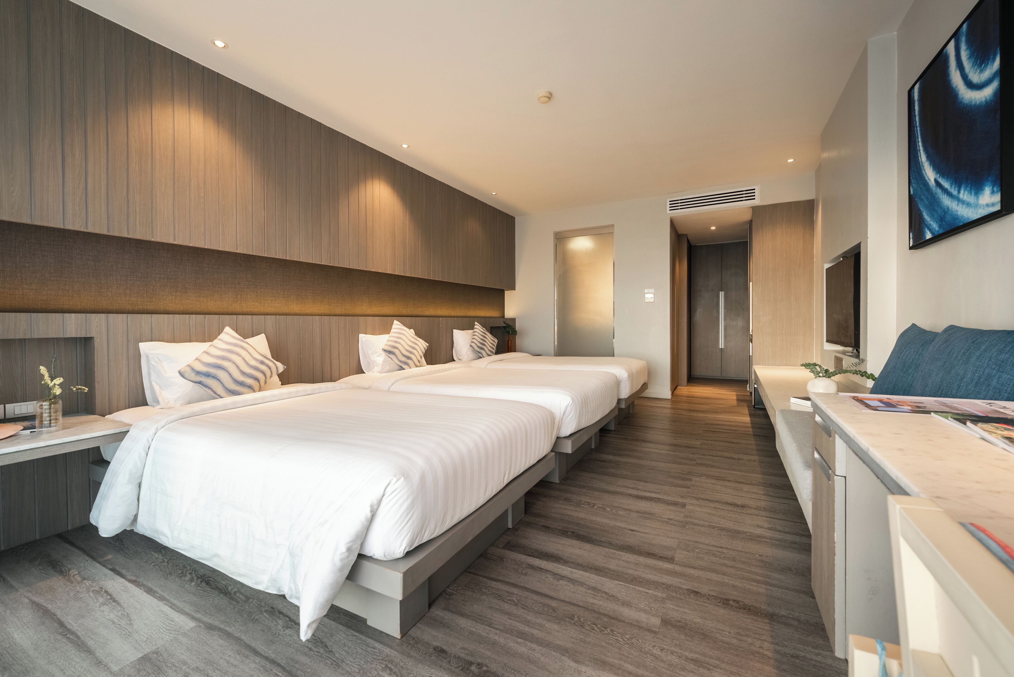 A modern hotel room with two beds, a desk, and a large painting on the wall.