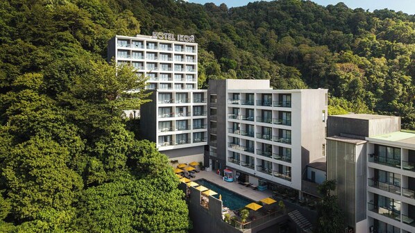 A hotel with multiple floors, a swimming pool, and lush greenery surrounding it. - Hotel IKON Phuket (Karon)