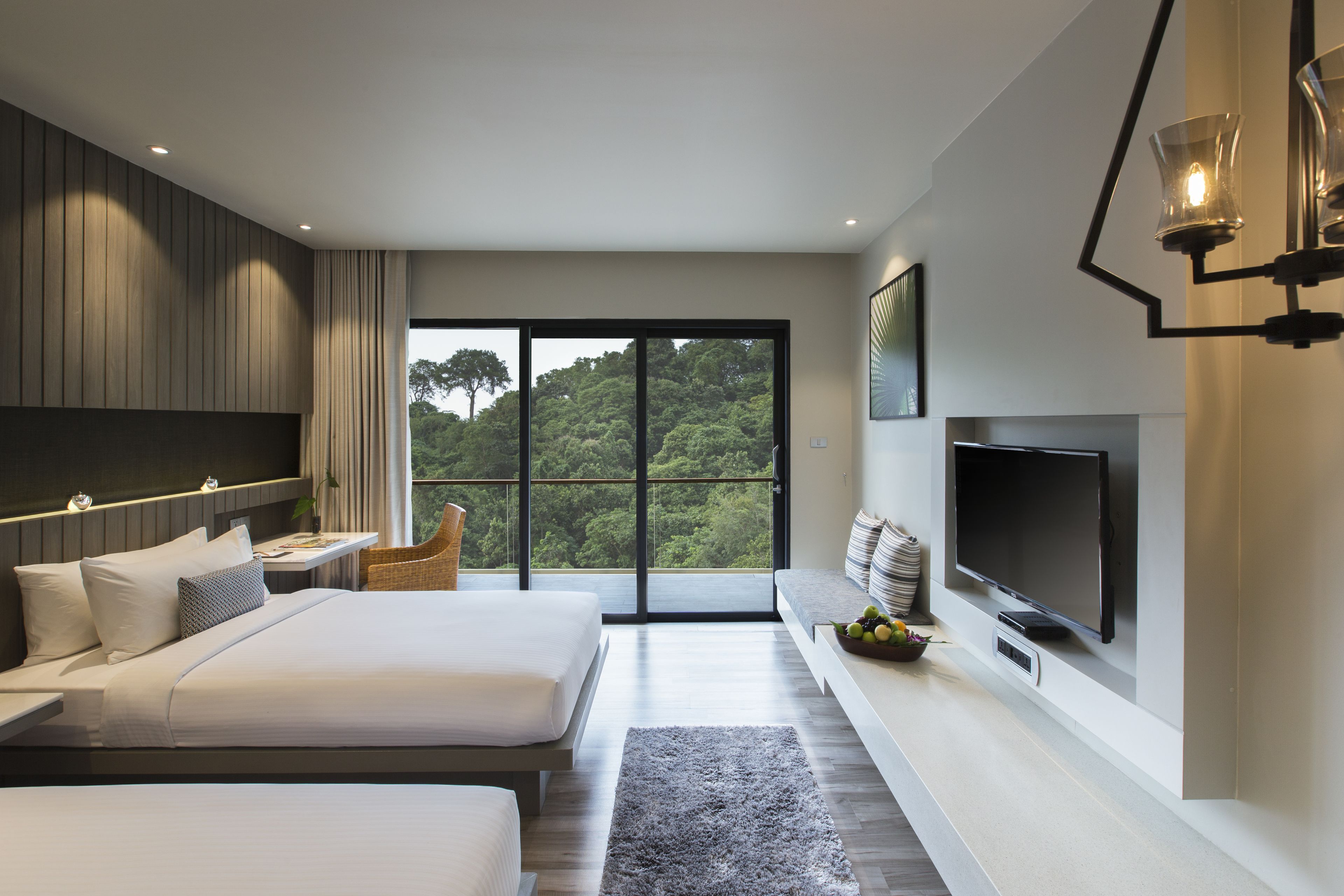 A modern hotel room with two beds, a large TV, and a balcony with a view of the forest.